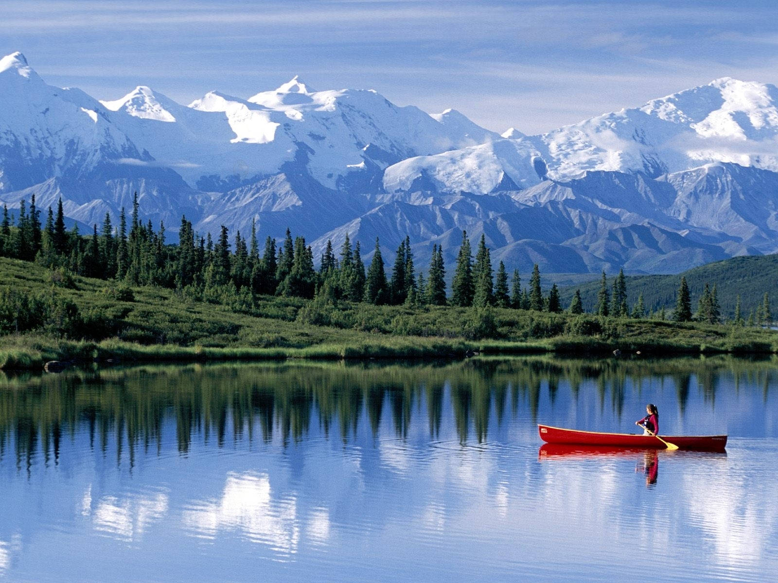 Lake 桌布 壁紙 — 一位孤獨的划艇者乘著紅色獨木舟，在如鏡的湖面上滑行，湖面映照出白雪覆蓋的山峰和常綠森林，上方是清澈的藍天。
