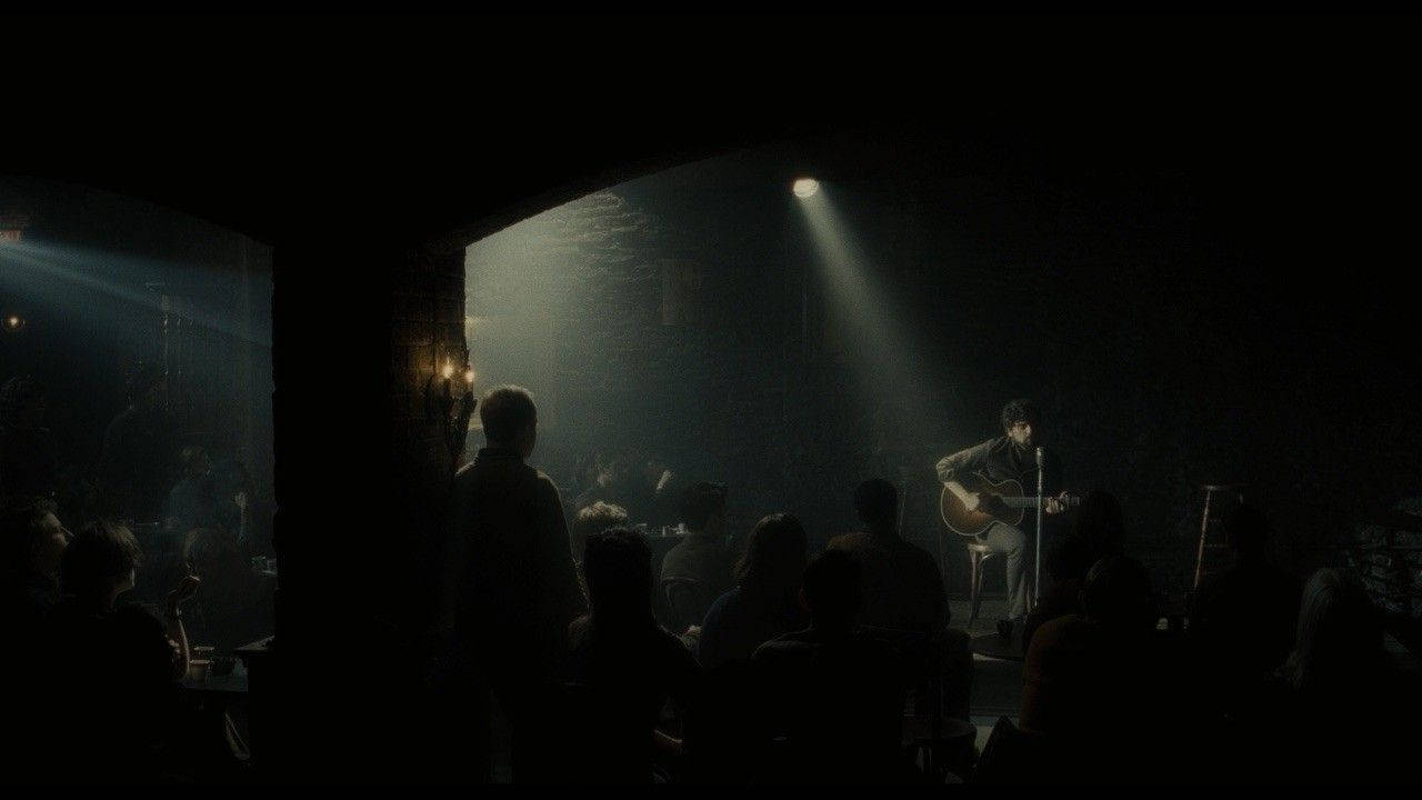 inside llewyn davis 桌布 壁紙 — 一位孤獨的吉他手在昏暗的親密場地中，於單一聚光燈下表演，觀眾以剪影呈現。