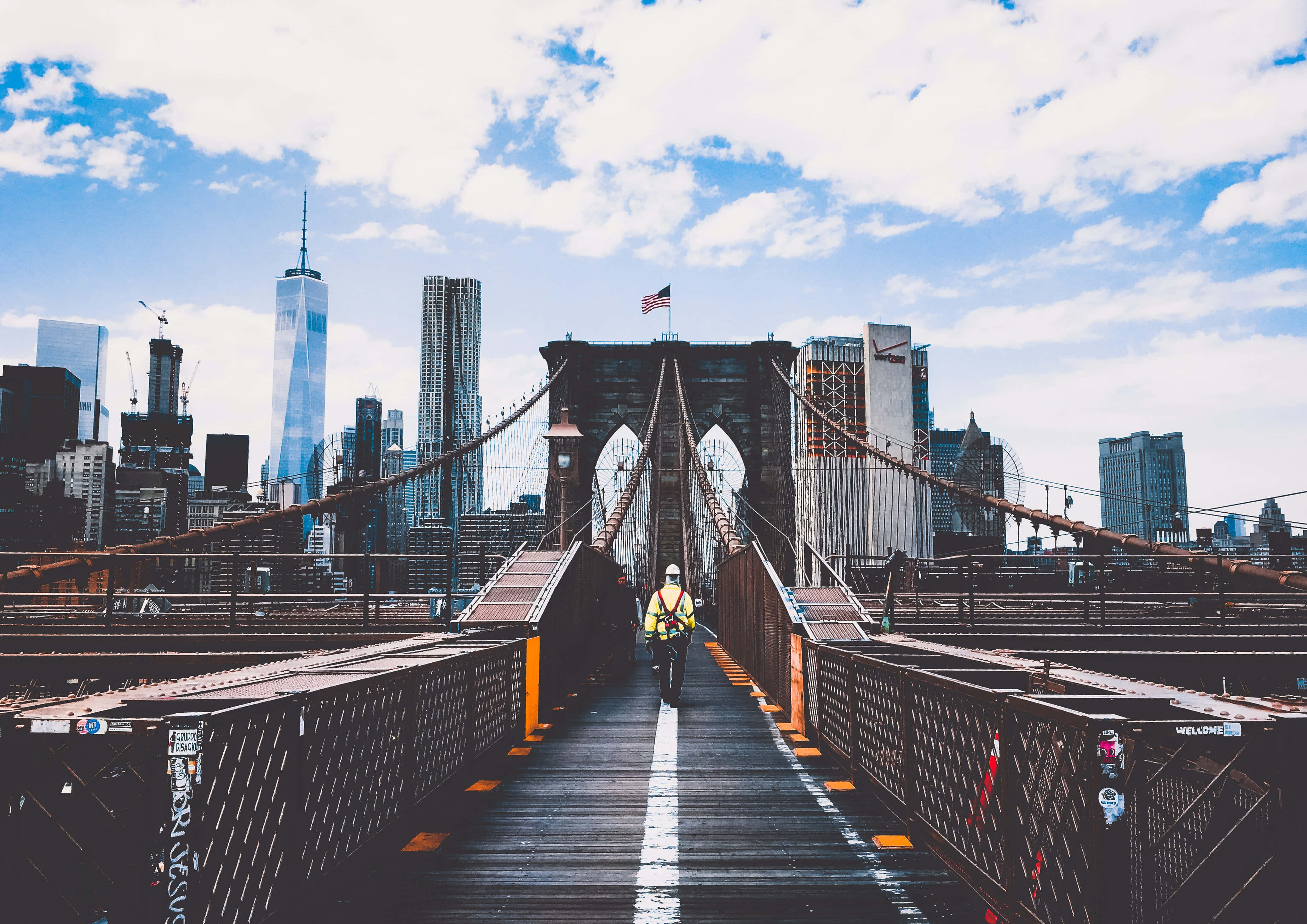 New York City Landscape 桌布 壁紙 — 一位孤獨的單車手在點綴著蓬鬆白雲的明亮藍天下，踩著踏板穿過布魯克林大橋。