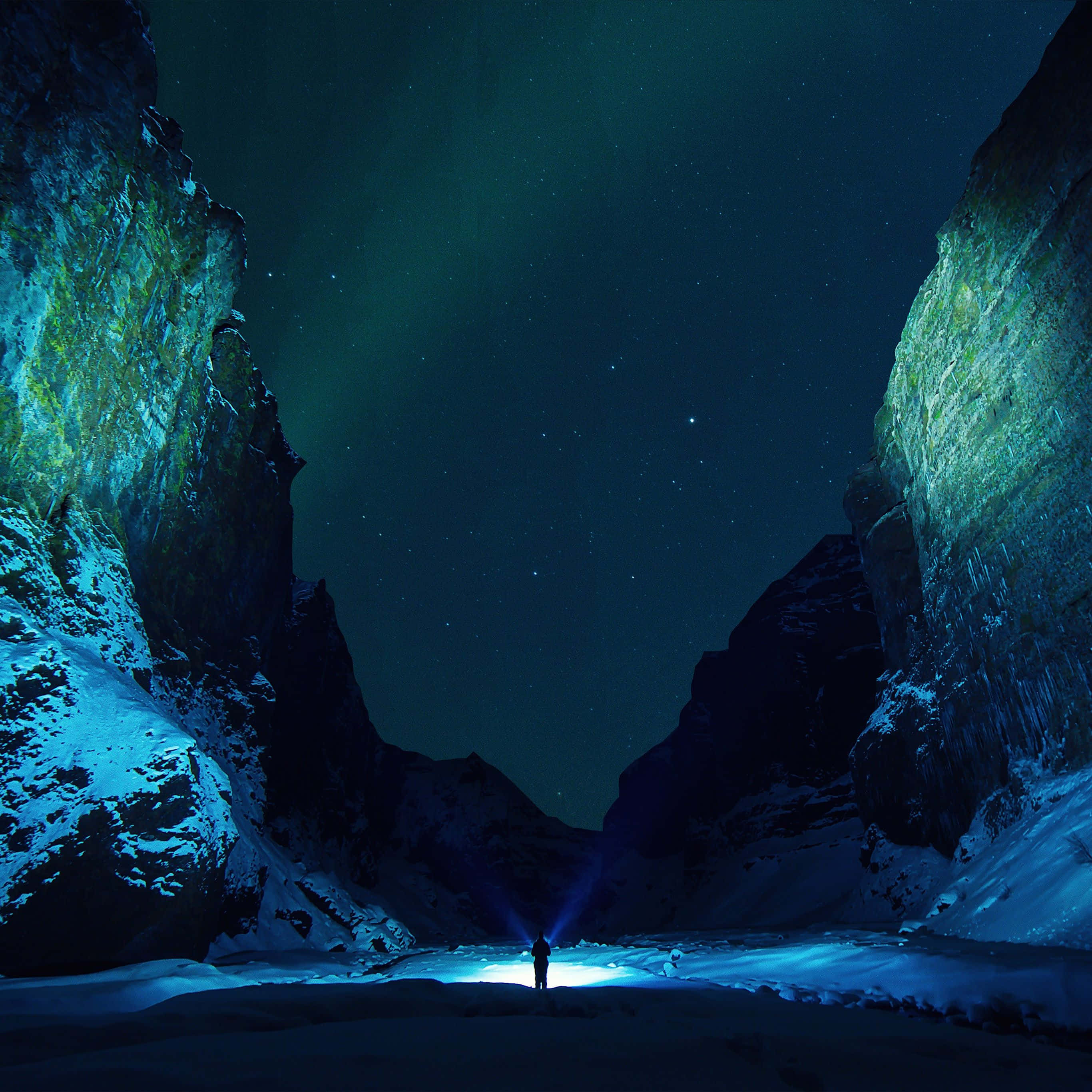 黑暗自然 桌布 壁紙 — 一位孤獨的徒步旅行者夜晚站在積雪的山峽谷中，將手電筒照向帶有微弱極光的星空。