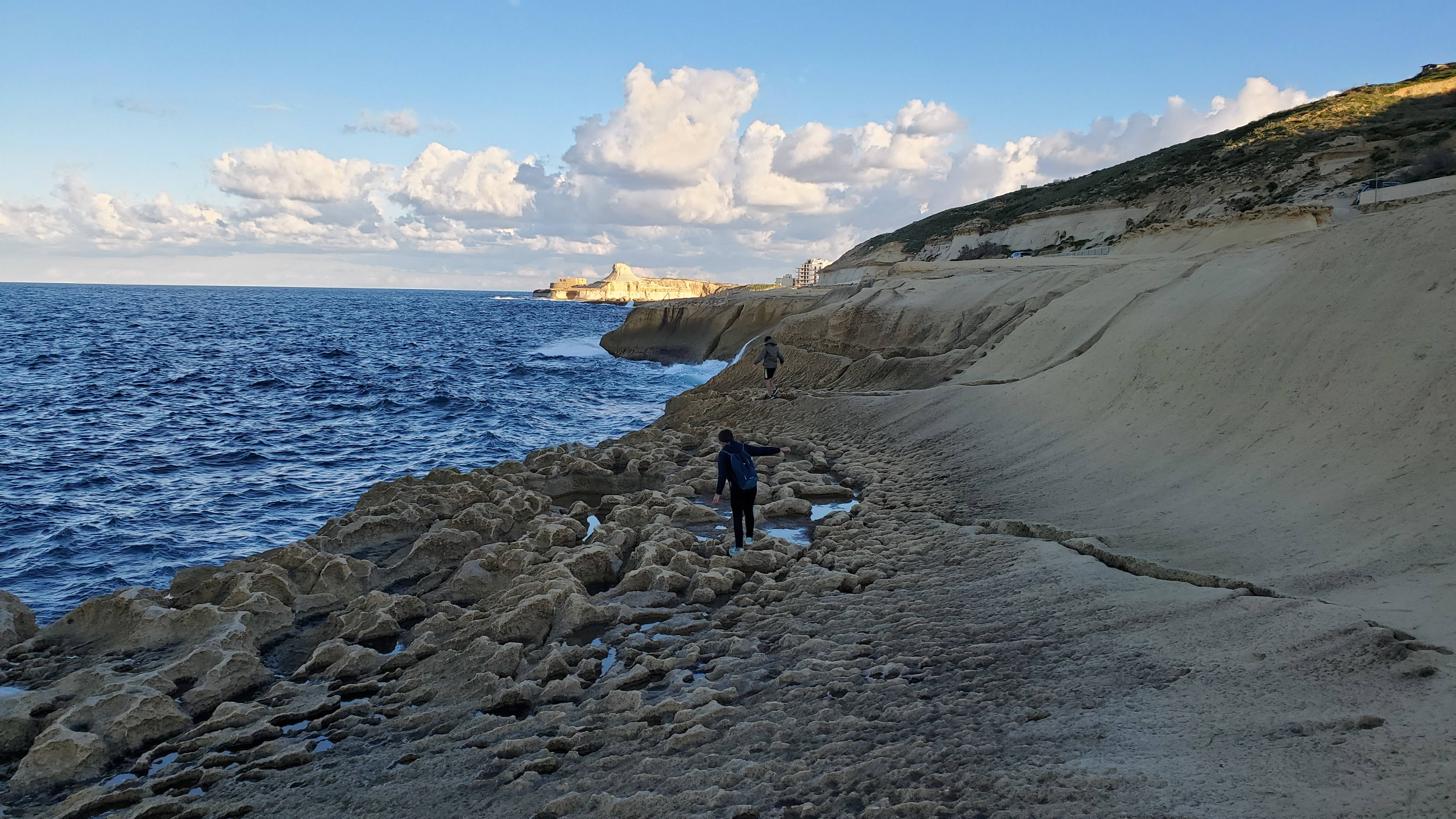 Malta 桌布 壁紙 — 一位孤獨的徒步者沿著崎嶇的海岸懸崖小徑行走，旁邊是深藍色的海洋，天空部分多雲。