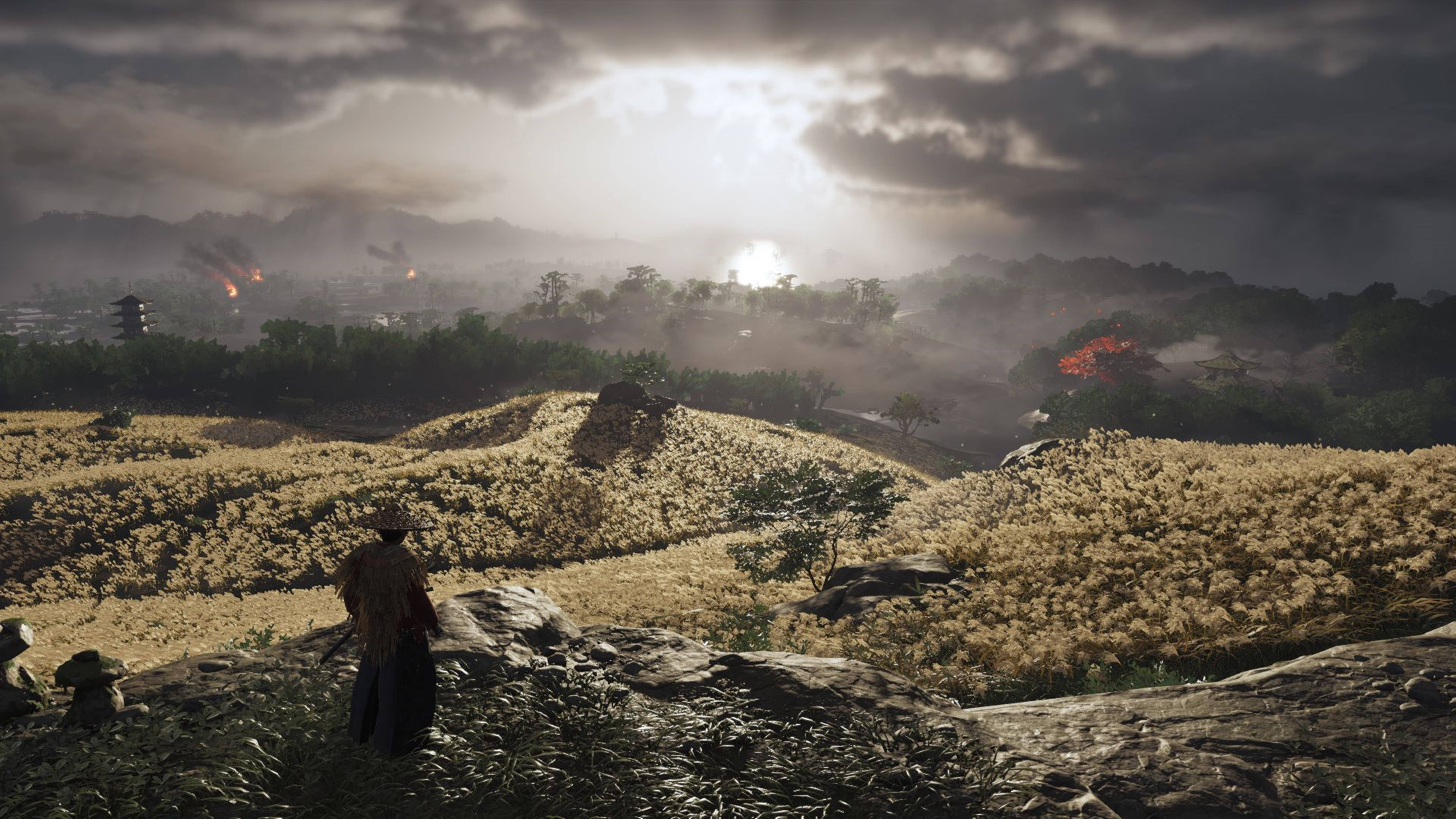 Ghost Of Tsushima 桌布 壁紙 — 一位孤獨的戰士站在岩石山丘上，俯瞰霧氣瀰漫的山谷，遠處有火光和一座寶塔，天空風雨欲來。