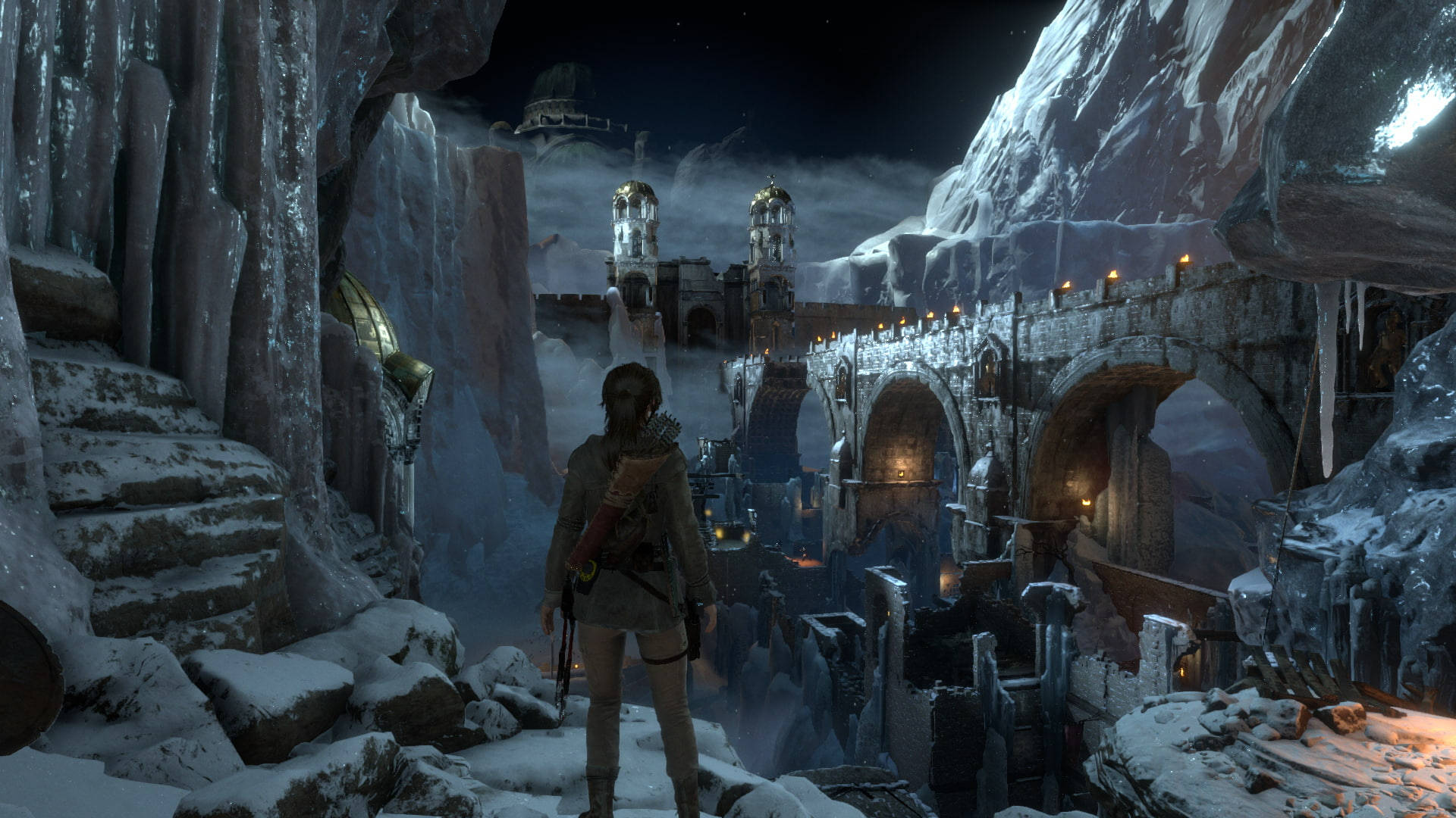 Rise Of The Tomb Raider 桌布 壁紙 — 一位孤獨的探險家站在積雪的懸崖上，俯瞰著一座被溫暖燈籠照亮、星空下的冰凍古代遺跡。