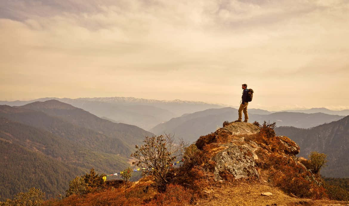 Travel Desktop 桌布 壁紙 — 一位孤獨的揹著背包的徒步旅行者站在岩石山脊上，俯瞰著層層疊疊的森林山谷，天空籠罩著朦朧的金色。