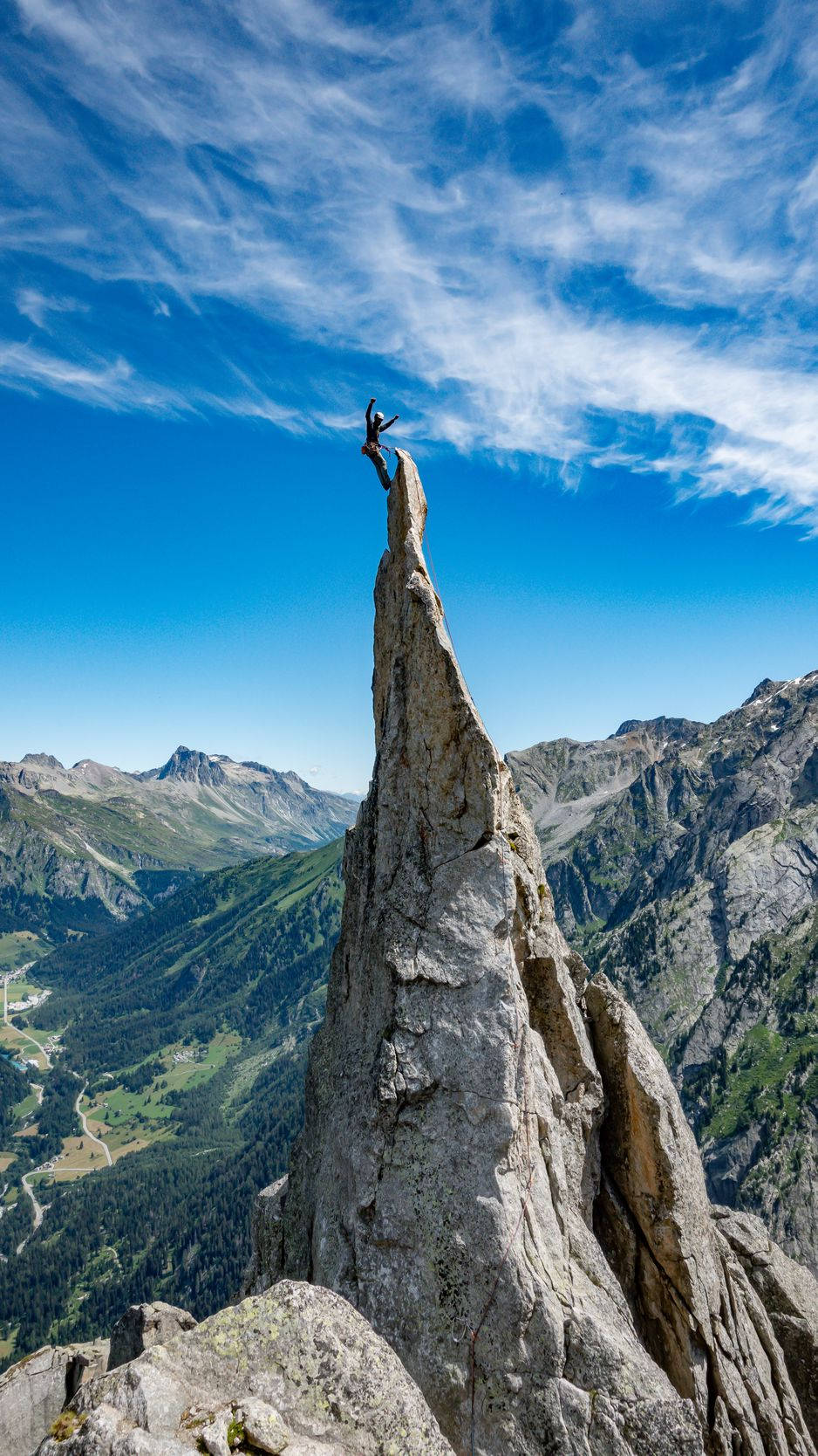 Climbing 桌布 壁紙 — 一位孤獨的攀岩者勝利地站在崎嶇的山峰頂端，頭頂是廣闊的藍天和縷縷白雲。