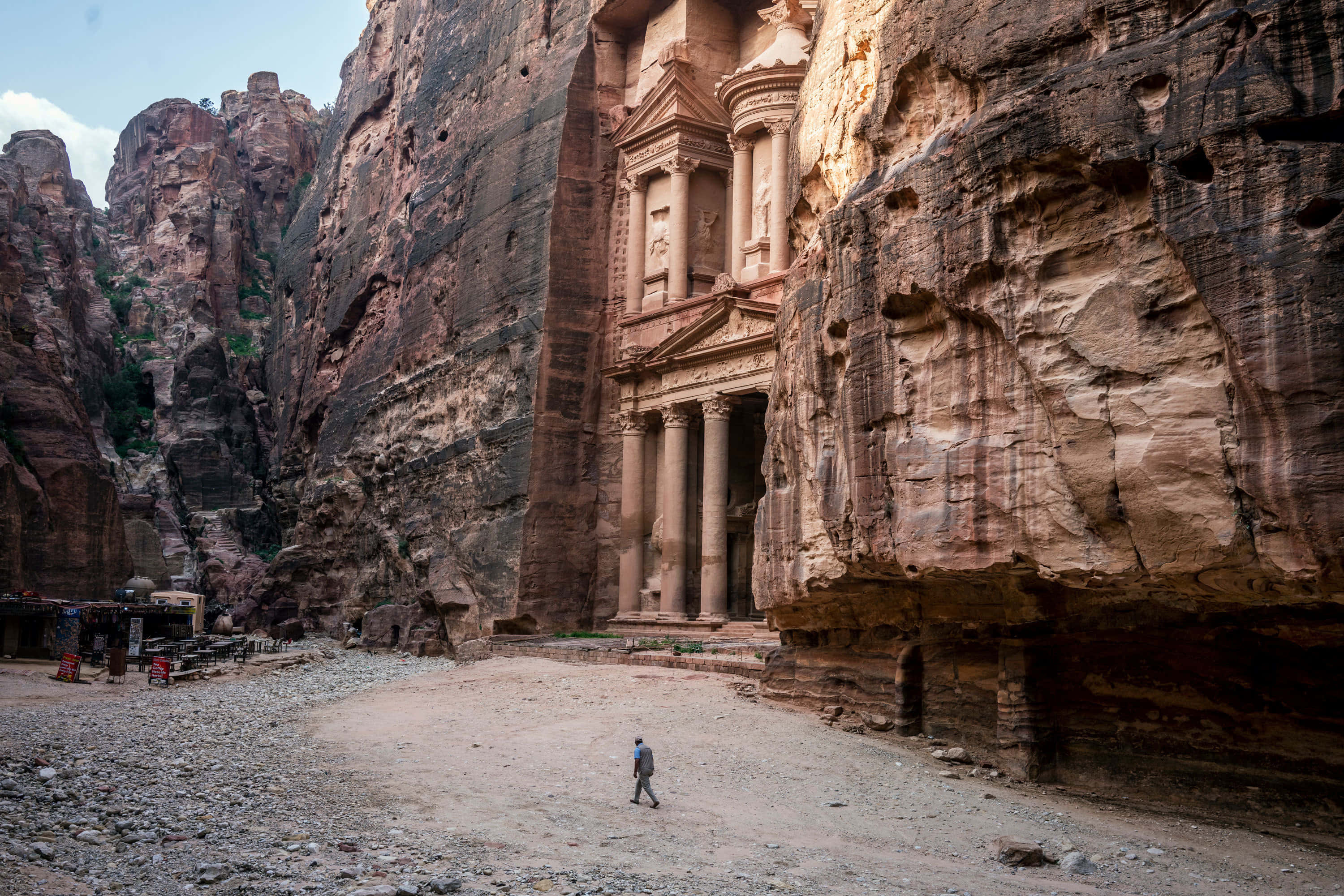 Jordan 桌布 壁紙 — 一位孤獨的旅行者走向佩特拉宏偉、雕刻精美的寶庫立面，該立面雕刻在高聳的玫瑰色砂岩懸崖上。