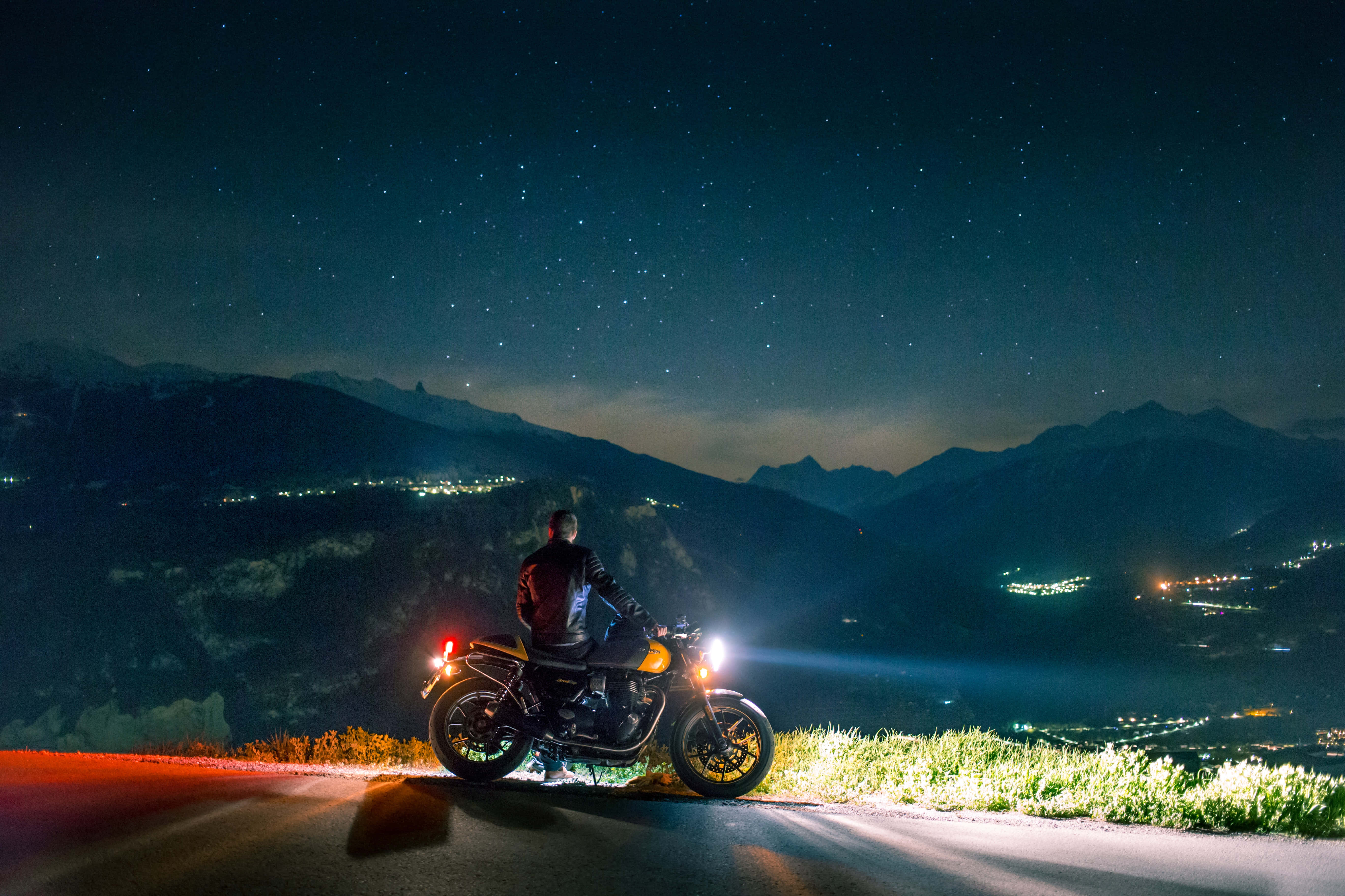 biker 桌布 壁紙 — 一位孤獨的機車騎士在星空下的夜晚山路上暫停，遠方的山谷燈光在下方閃爍。