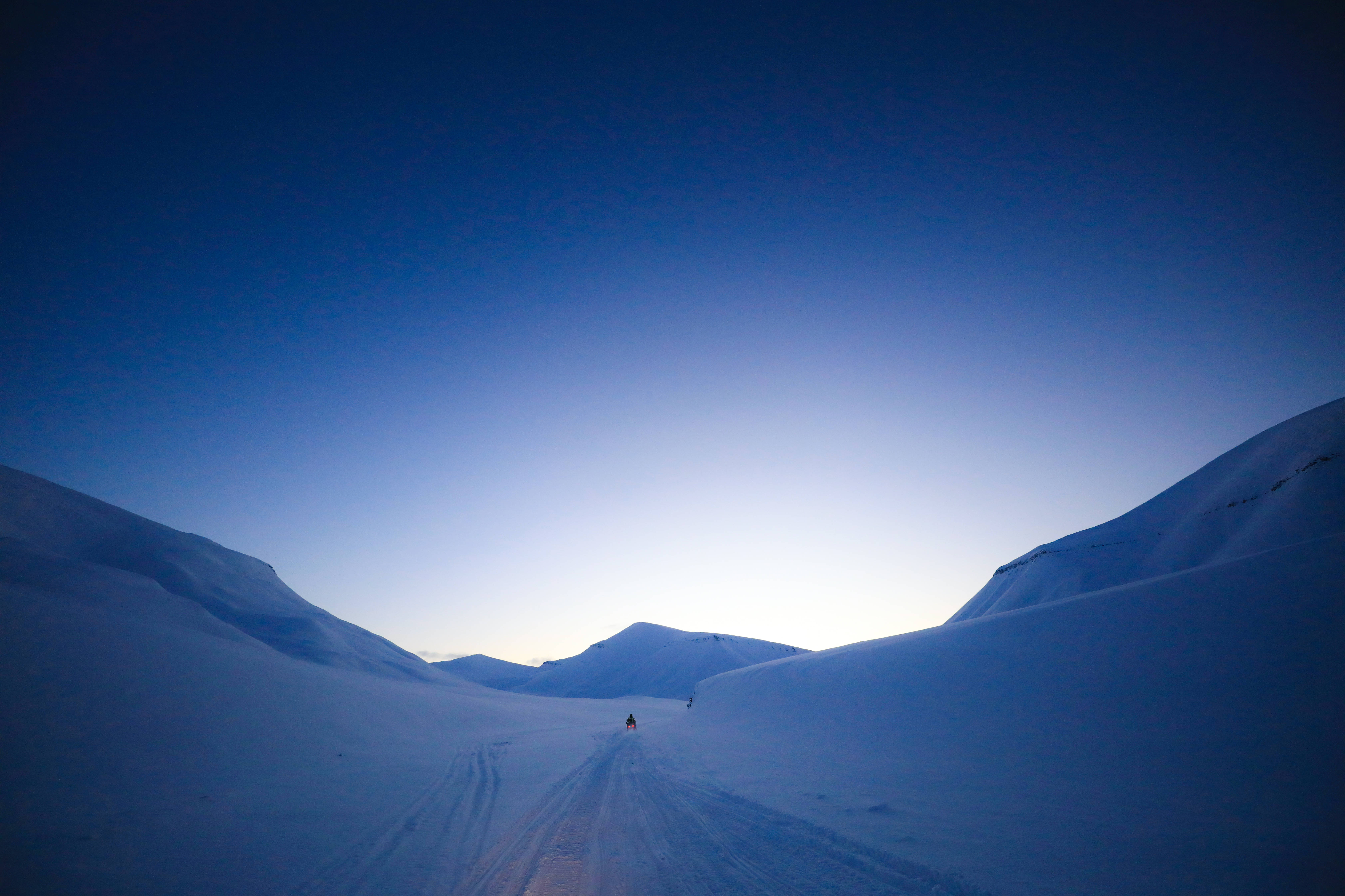 Svalbard 桌布 壁紙 — 一位孤獨的滑雪者在廣闊的暮色天空下滑過白雪覆蓋的山谷，天空呈現深藍色漸層。