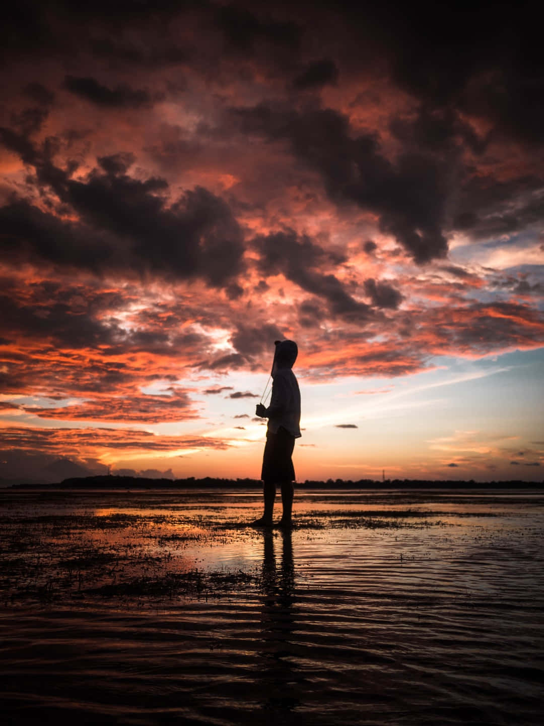 Alone 桌布 壁紙 — 一位孤獨的漁夫在淺水中以剪影站立，背景是帶有戲劇性雲彩的熾熱日落天空。