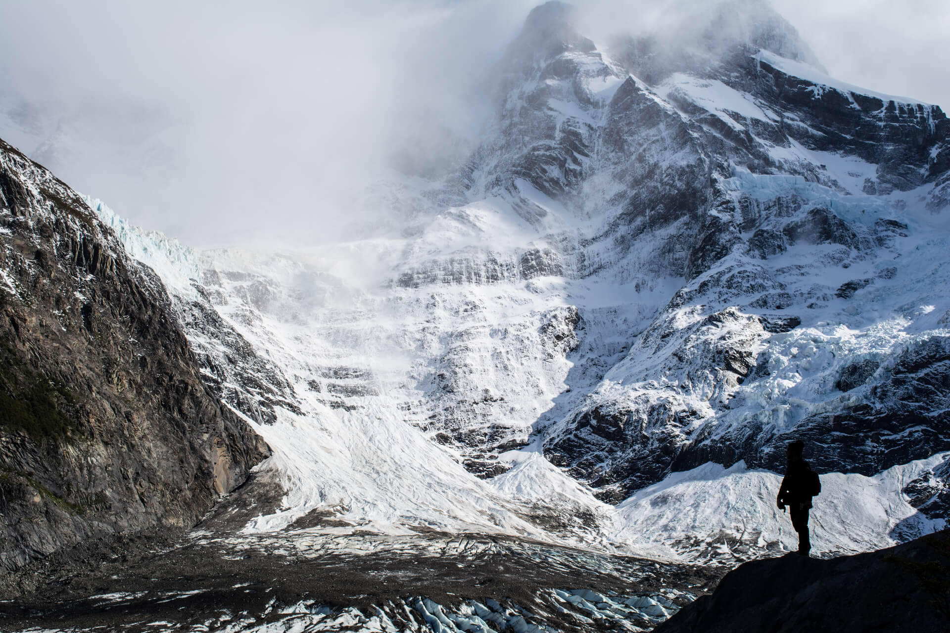 South America 桌布 壁紙 — 一位孤獨的登山者站在廣闊的冰川和被迷霧籠罩的積雪山峰前，形成剪影。