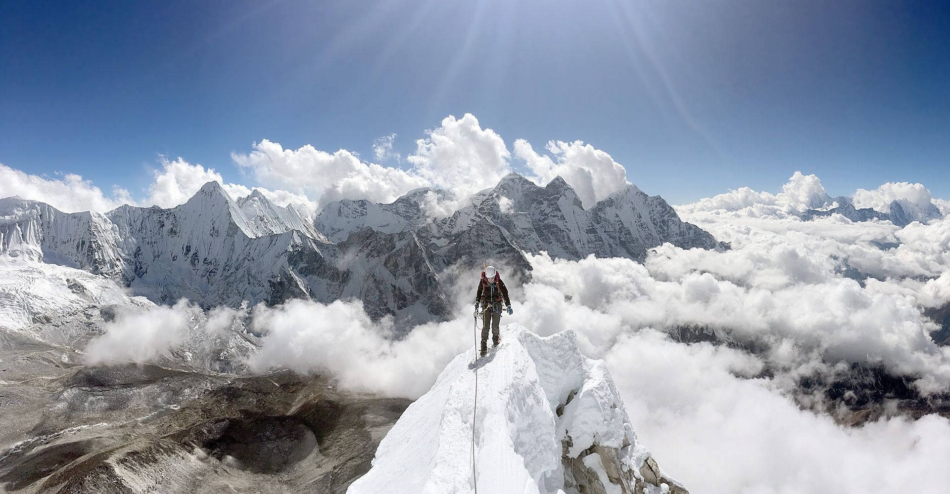 攀爬 桌布 壁紙 — 一位孤獨的登山者站在白雪覆蓋的山頂上，下方是雲海，上方是明亮的藍天。