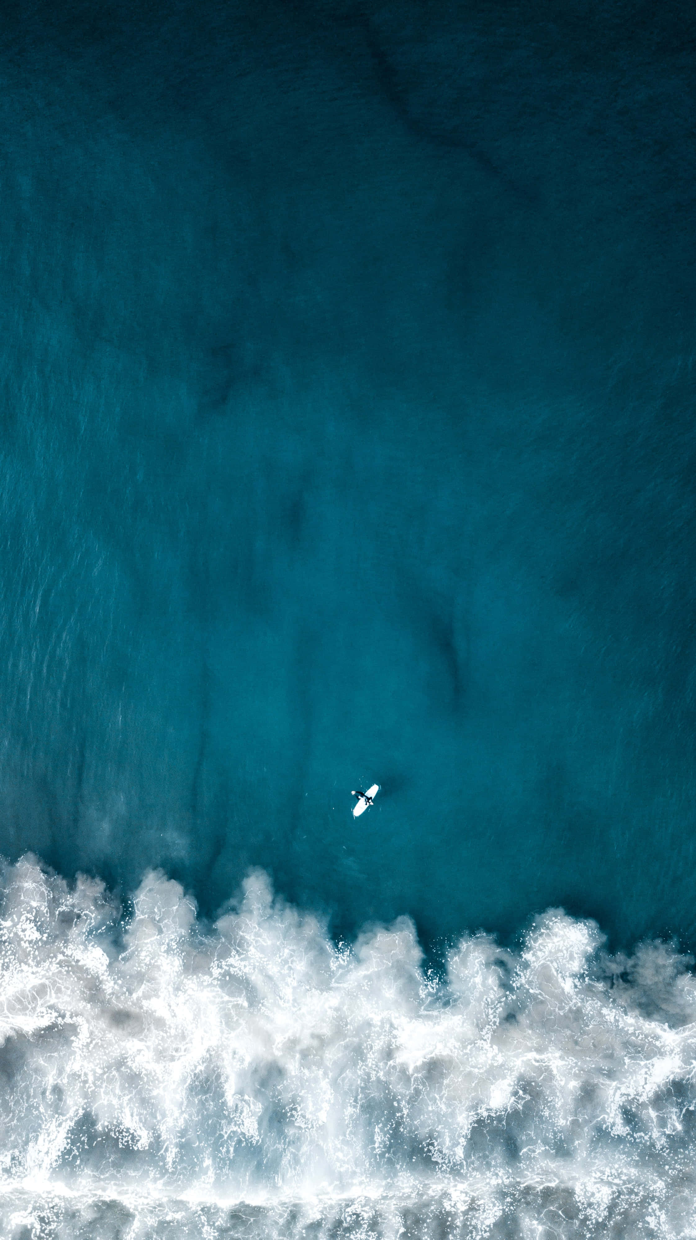 iPhone 桌布 壁紙 — 一位孤獨的衝浪者在碧綠色的海浪上滑行，白色泡沫從空中視角在下方破碎。