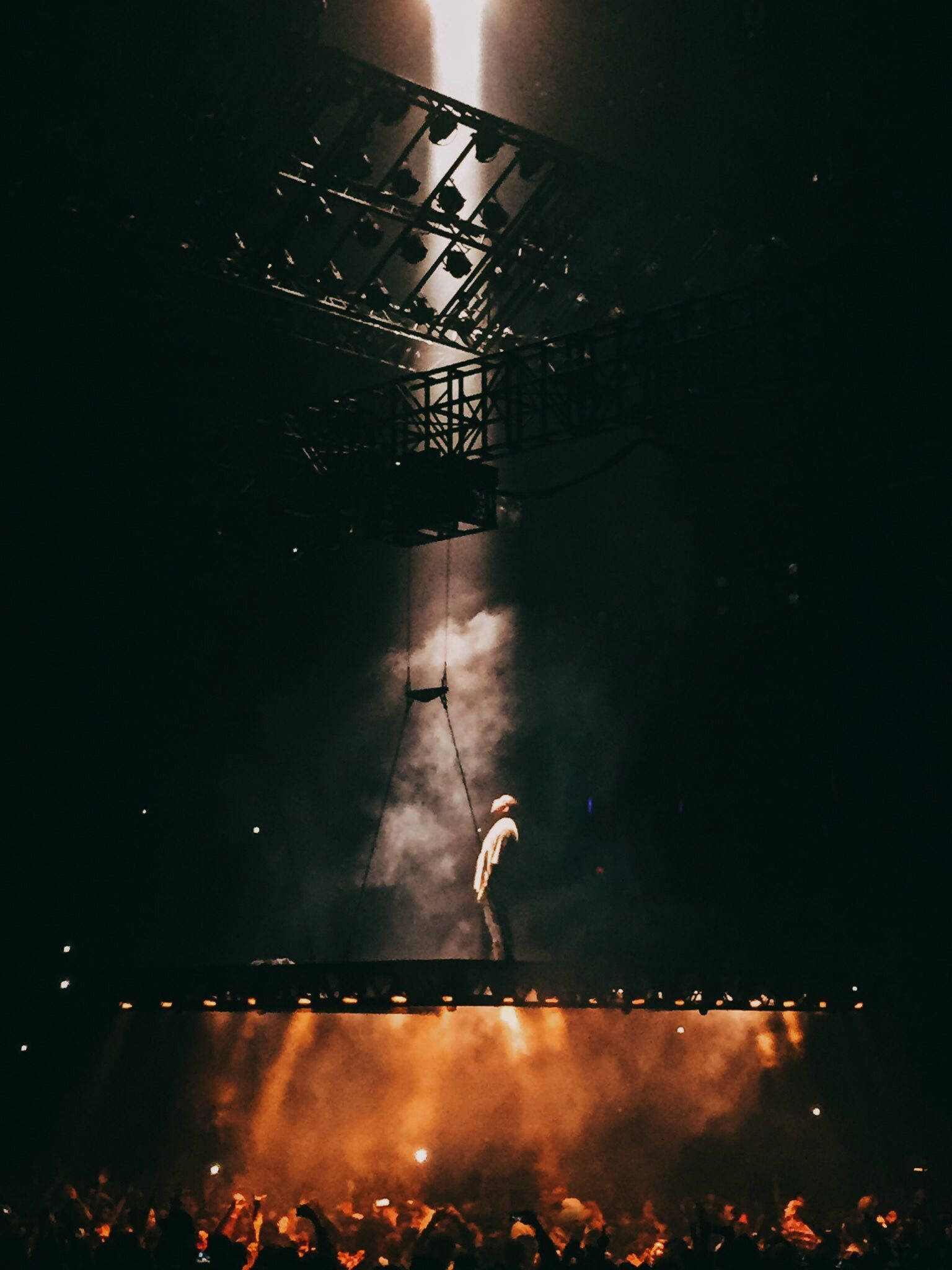 Kanye 桌布 壁紙 — 一位孤獨的表演者站在燈光昏暗的舞台上，沐浴在溫暖的橙色燈光和煙霧中，而人群在下方觀看。