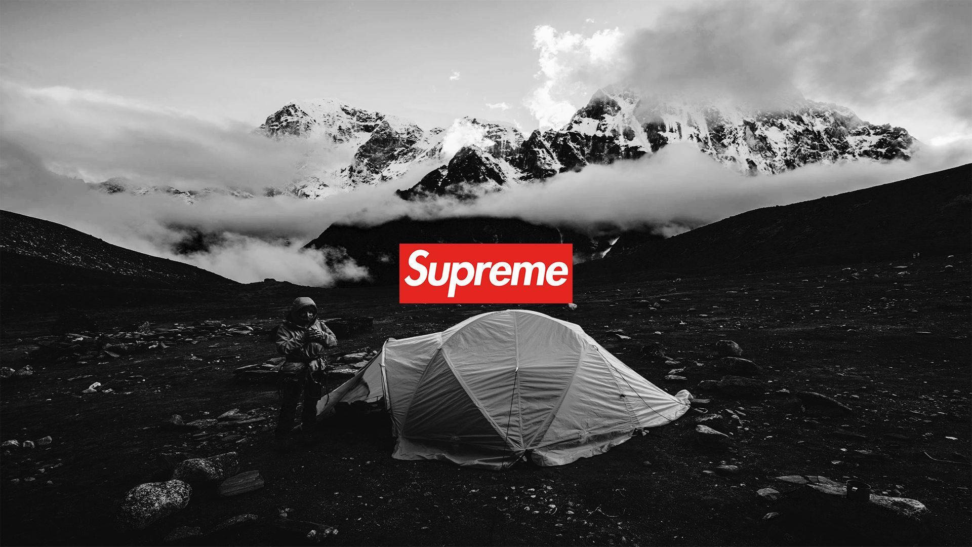 Cool Supreme 桌布 壁紙 — 一位孤獨的遠足者在一個荒涼的山谷中搭建帳篷，山谷中有積雪的山峰和雲朵，下方是一個大膽的紅色Supreme標誌。