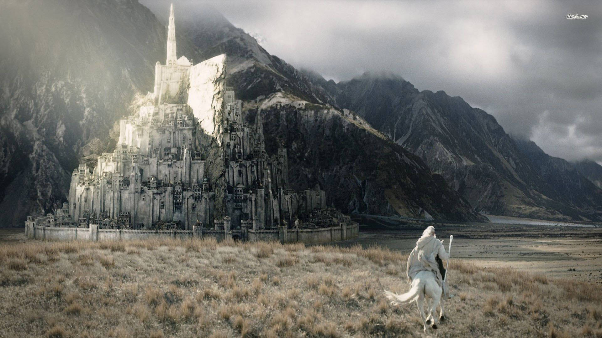 Lotr 桌布 壁紙 — 一位孤獨的騎手騎著白馬，奔向一座雄偉的石頭堡壘，該堡壘坐落在迷霧繚繞的山頂上，天空風雨交加。