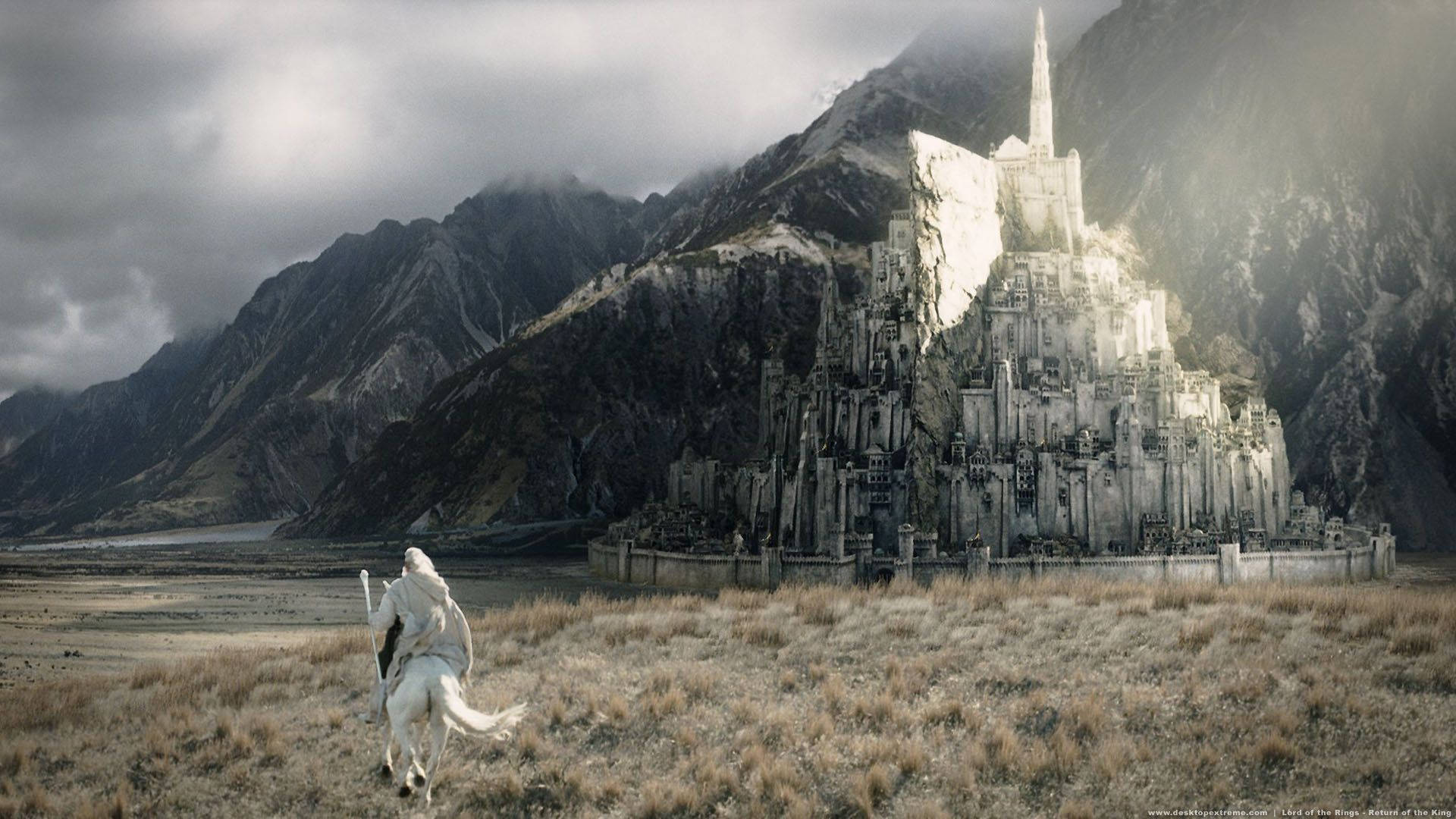 Lotr 桌布 壁紙 — 一位孤獨的騎手騎著白馬奔馳過荒蕪的平原，朝向一座雄偉的古老石頭堡壘，該堡壘坐落在迷霧繚繞的山脈頂峰，天空風暴肆虐。