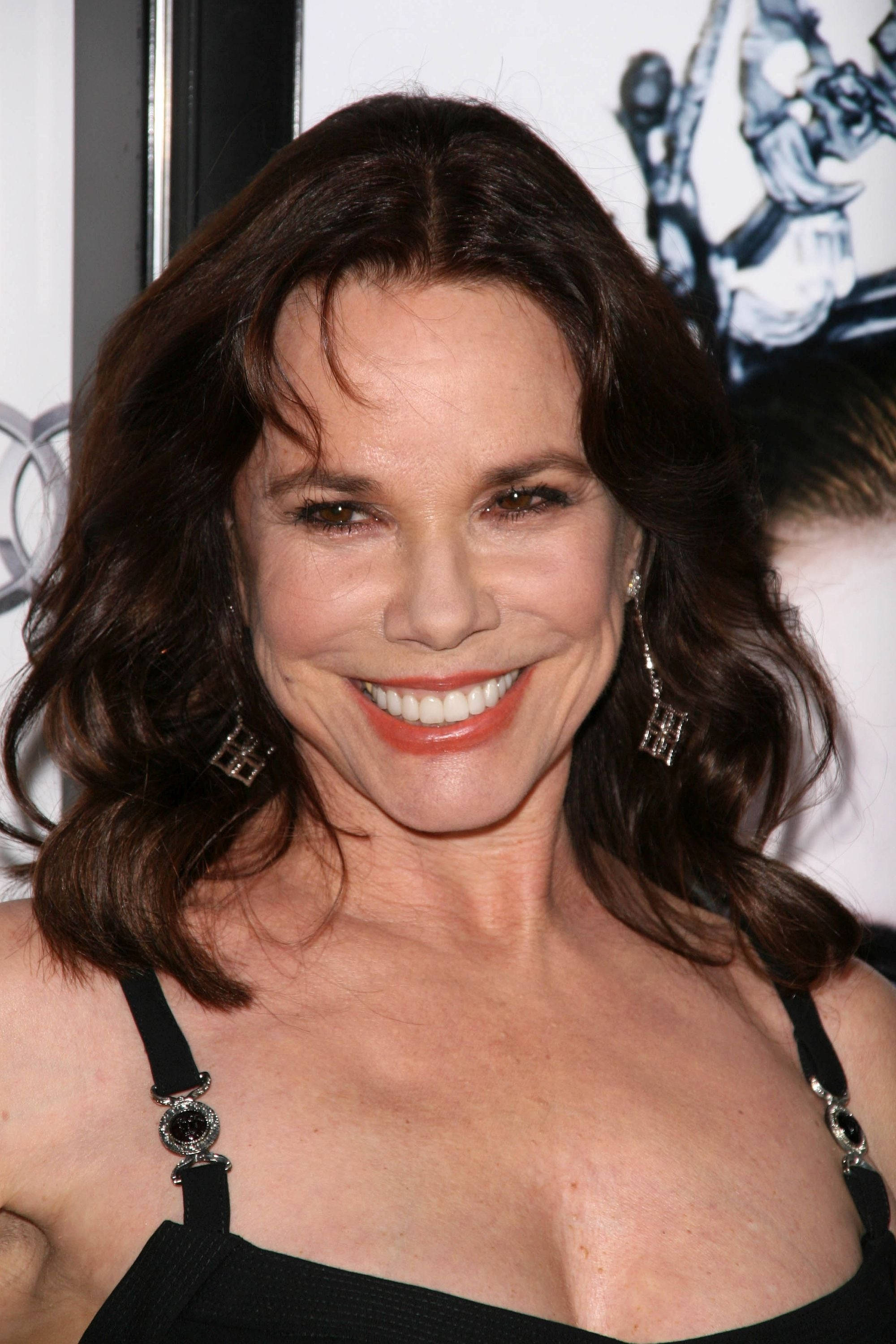 Celebrity 桌布 壁紙 — 一位容光煥發、擁有波浪棕色長髮的女性，身穿黑色連衣裙和垂墜耳環，對著鏡頭燦爛微笑。