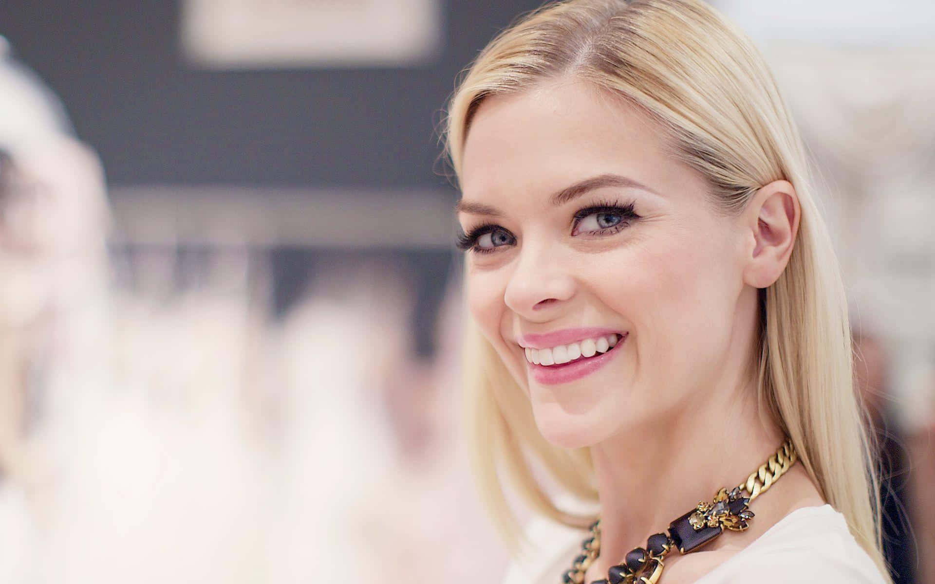 Jaime King 桌布 壁紙 — 一位容光煥發的金髮女性，擁有明亮的藍色眼睛，戴著金黑相間的項鍊，溫暖地微笑。