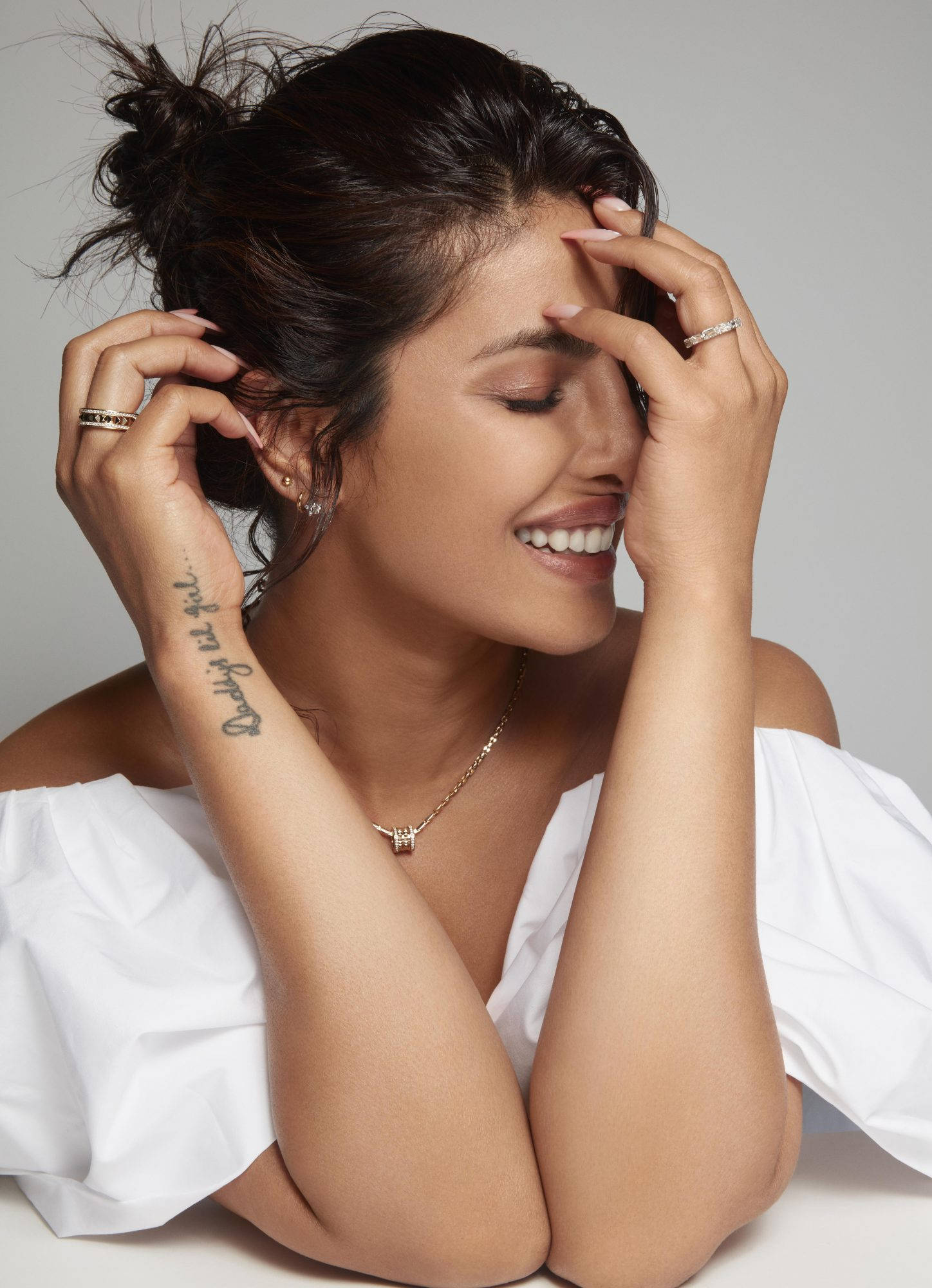 Priyanka 桌布 壁紙 — 一位容光煥發的黑髮女性，頭髮紮成凌亂的髮髻，微笑著溫暖地輕撫著飾有珠寶和可見刺青的臉龐和頸部。