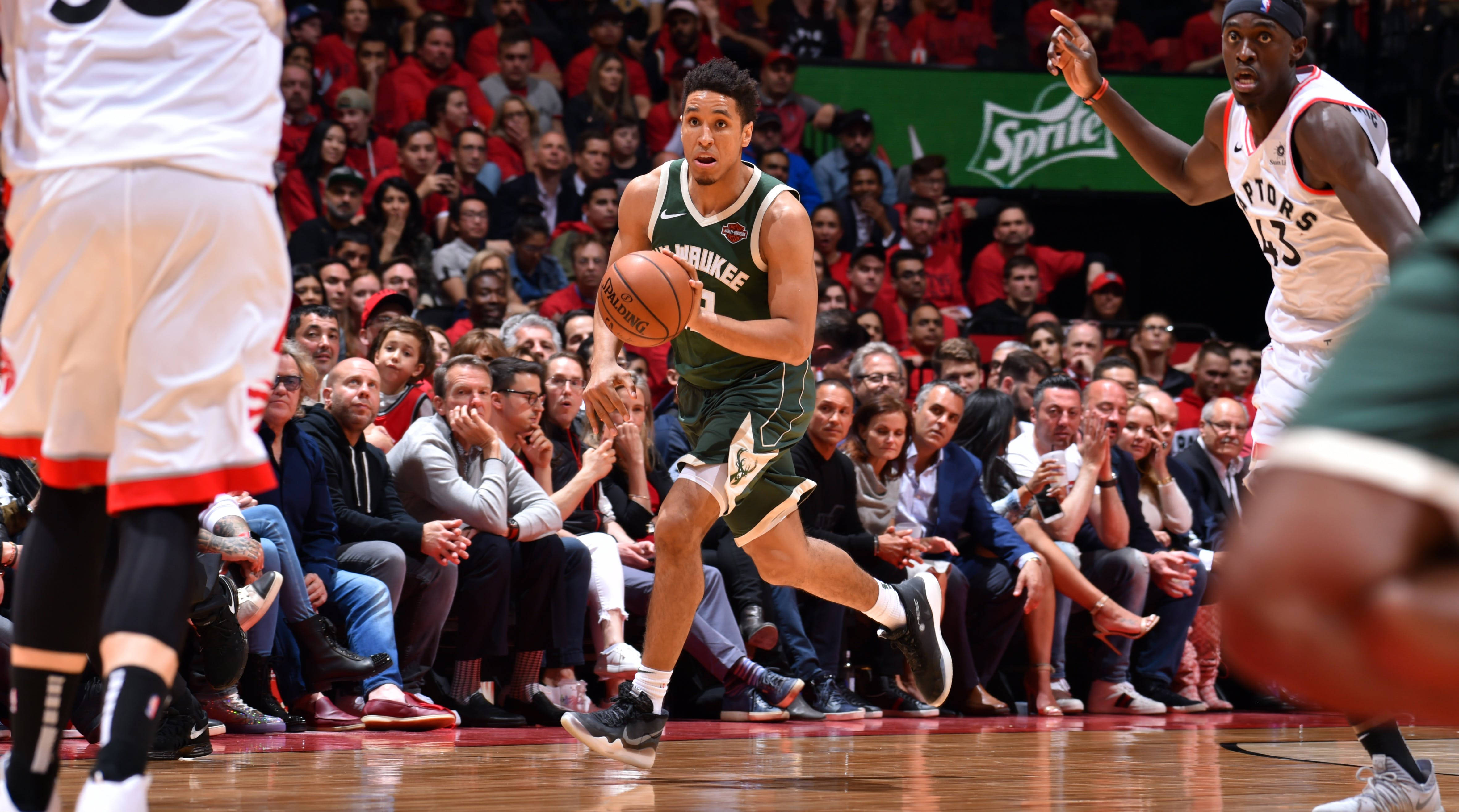 malcolm brogdon 桌布 壁紙 — 一位密爾瓦基公鹿隊球員在擠滿觀眾的籃球場上運球，同時受到防守。
