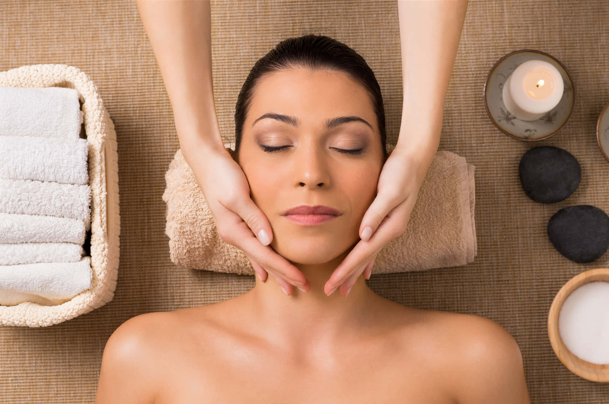 Massage 桌布 壁紙 — 一位寧靜的女性在一個寧靜的水療環境中接受面部按摩，周圍有蠟燭和石頭。