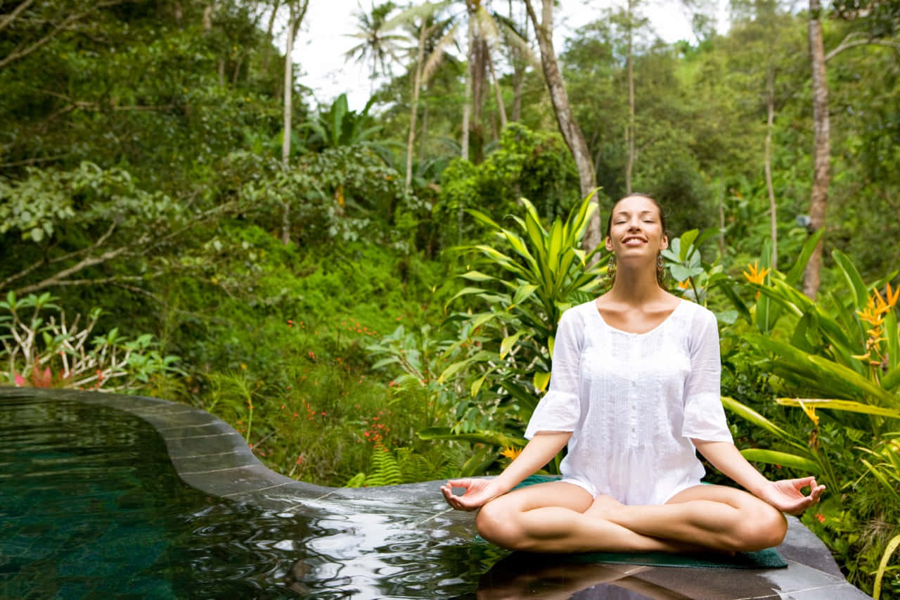 Eco-tourism 桌布 壁紙 — 一位寧靜的女性在叢林無邊際泳池邊以蓮花坐姿冥想，四周環繞著茂密的綠植。