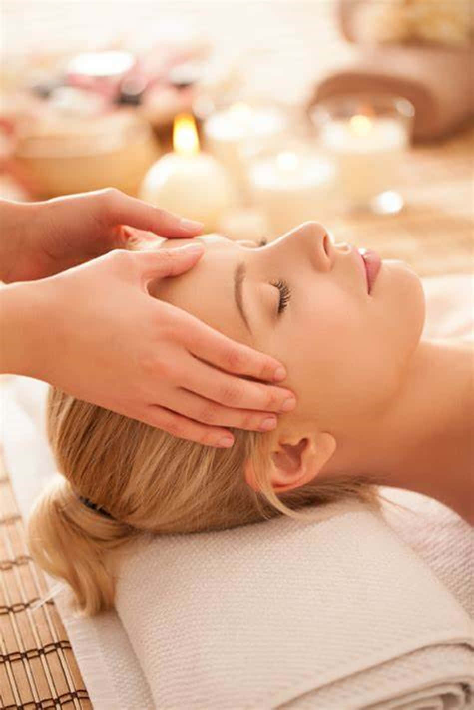Massage 桌布 壁紙 — 一位寧靜的女性在柔和燈光、燭光閃爍和溫暖色調的水療中心享受輕柔的面部按摩。