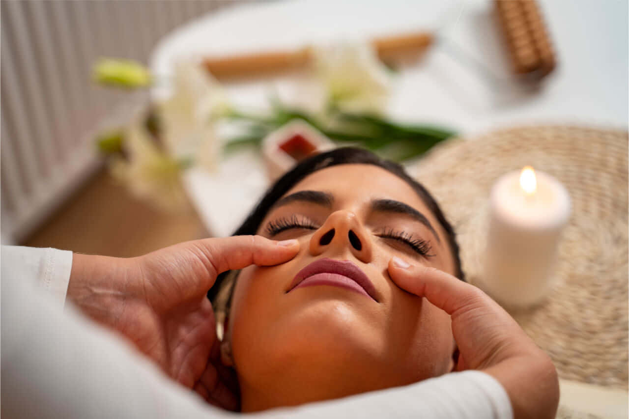 Massage 桌布 壁紙 — 一位寧靜的女性接受輕柔的手指面部按摩，點燃的蠟燭和白色百合營造出寧靜的水療氛圍。