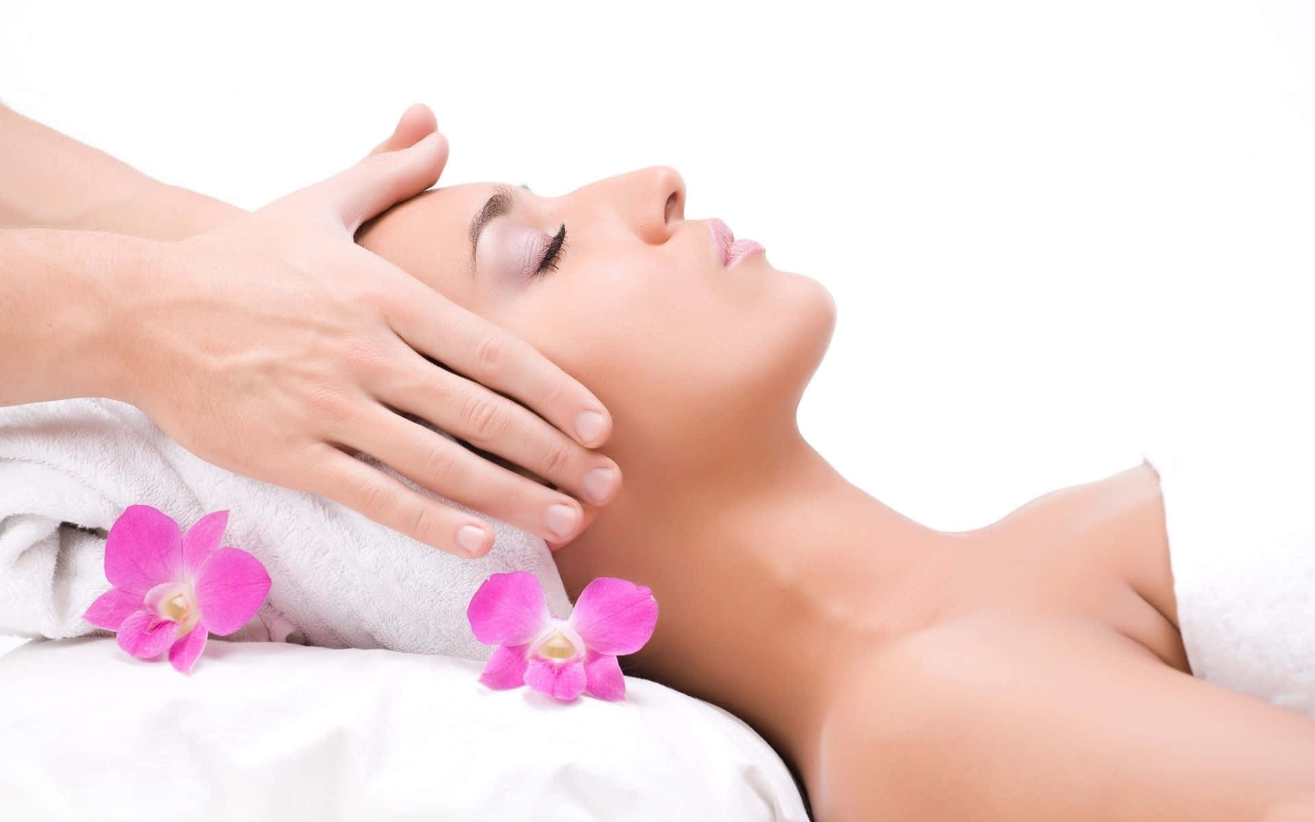 Massage 桌布 壁紙 — 一位寧靜的女性正在接受輕柔的臉部按摩，旁邊的白色毛巾上放著粉紅色的蘭花。