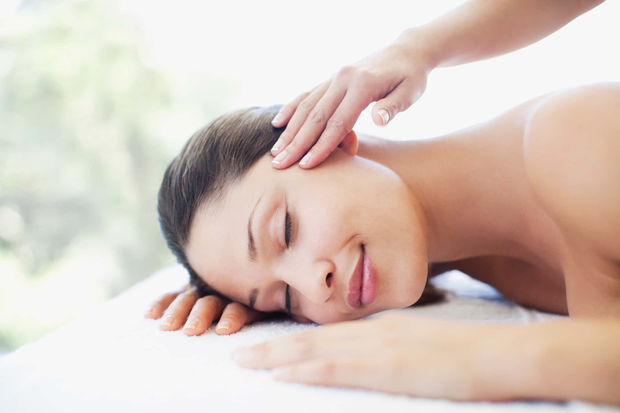 Massage 桌布 壁紙 — 一位寧靜的女性閉著眼睛，在明亮的SPA環境中，白色毛巾上享受輕柔的頭部按摩。