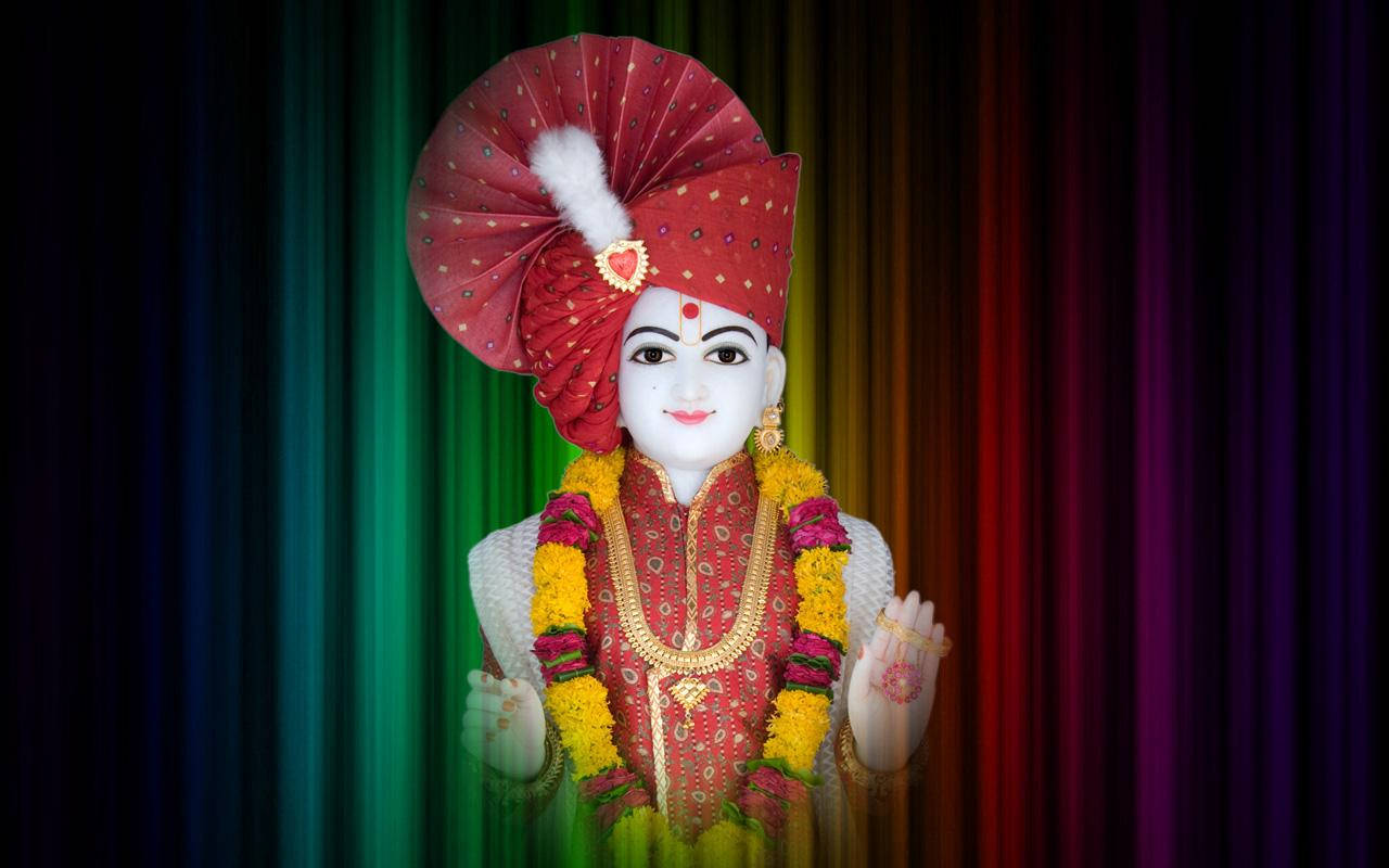 Swaminarayan 桌布 壁紙 — 一位寧靜的白臉神祇，身著紅金服飾，佩戴花環，站在鮮豔的彩虹簾幕前。