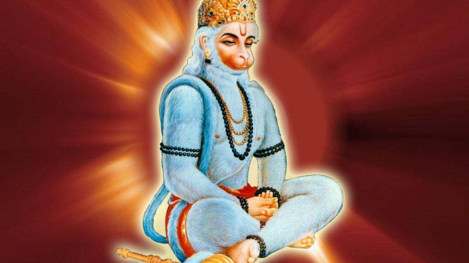 lord hanuman HD 桌布 壁紙 — 一位寧靜的藍皮膚猴神戴著金色皇冠，盤腿而坐，在發光的紅色背景前散發光芒。