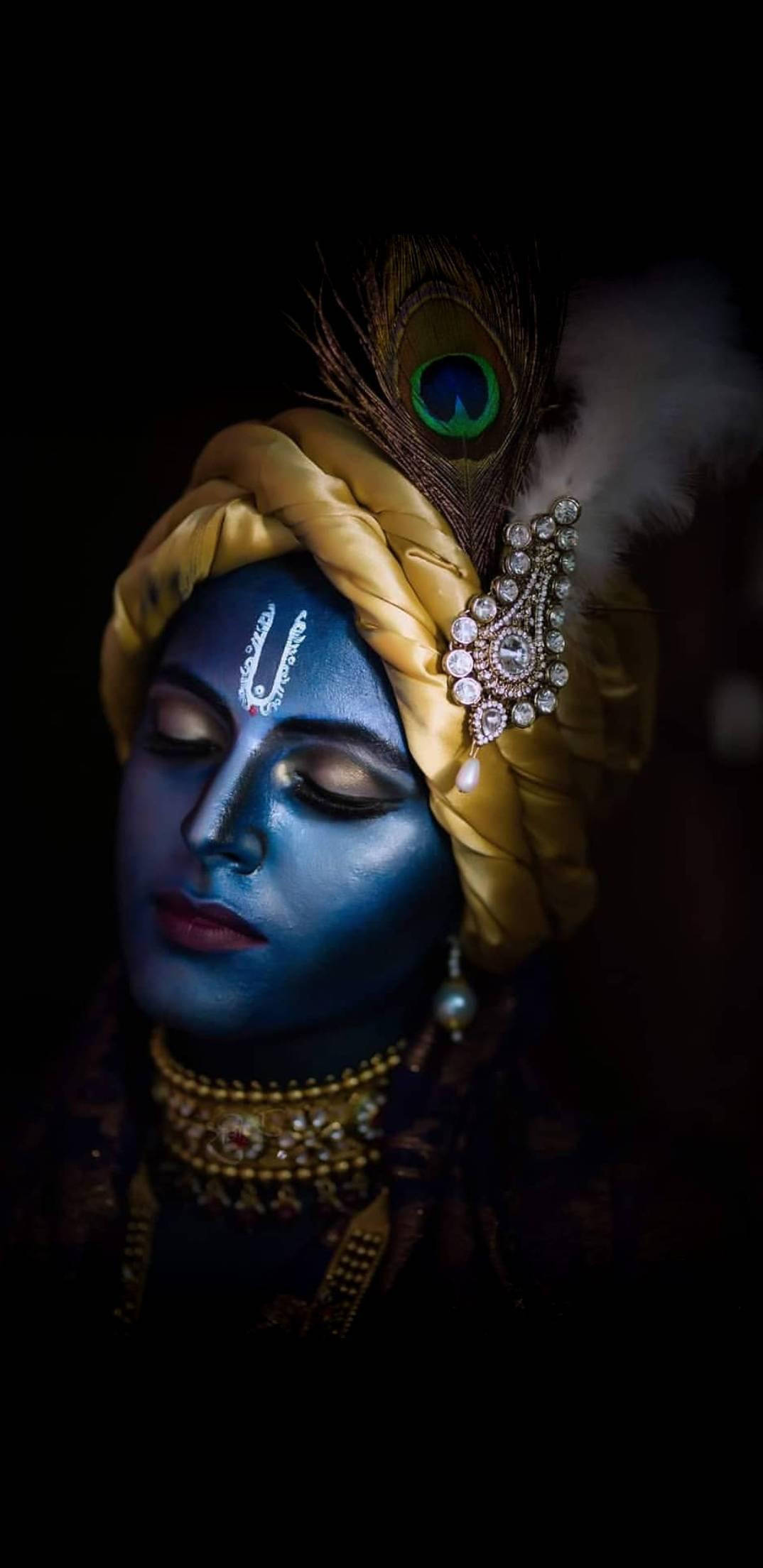 krishna phone 桌布 壁紙 — 一位寧靜的藍皮膚神祇，閉著眼睛，戴著金色珠寶和孔雀羽毛冠冕，背景為深色。