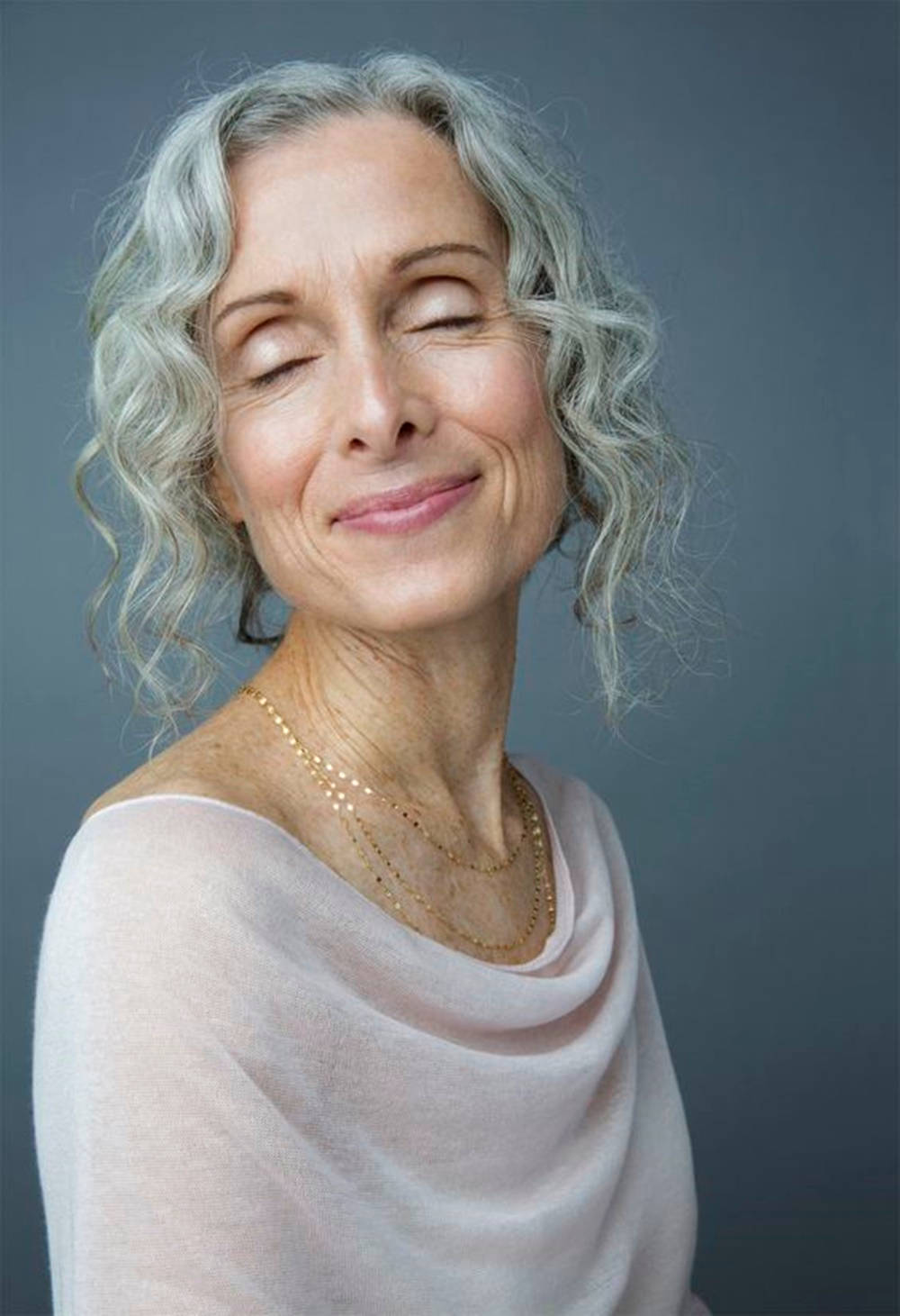 Grandma 桌布 壁紙 — 一位寧靜的銀色捲髮女性在柔和的灰色背景下閉著眼睛溫柔微笑。