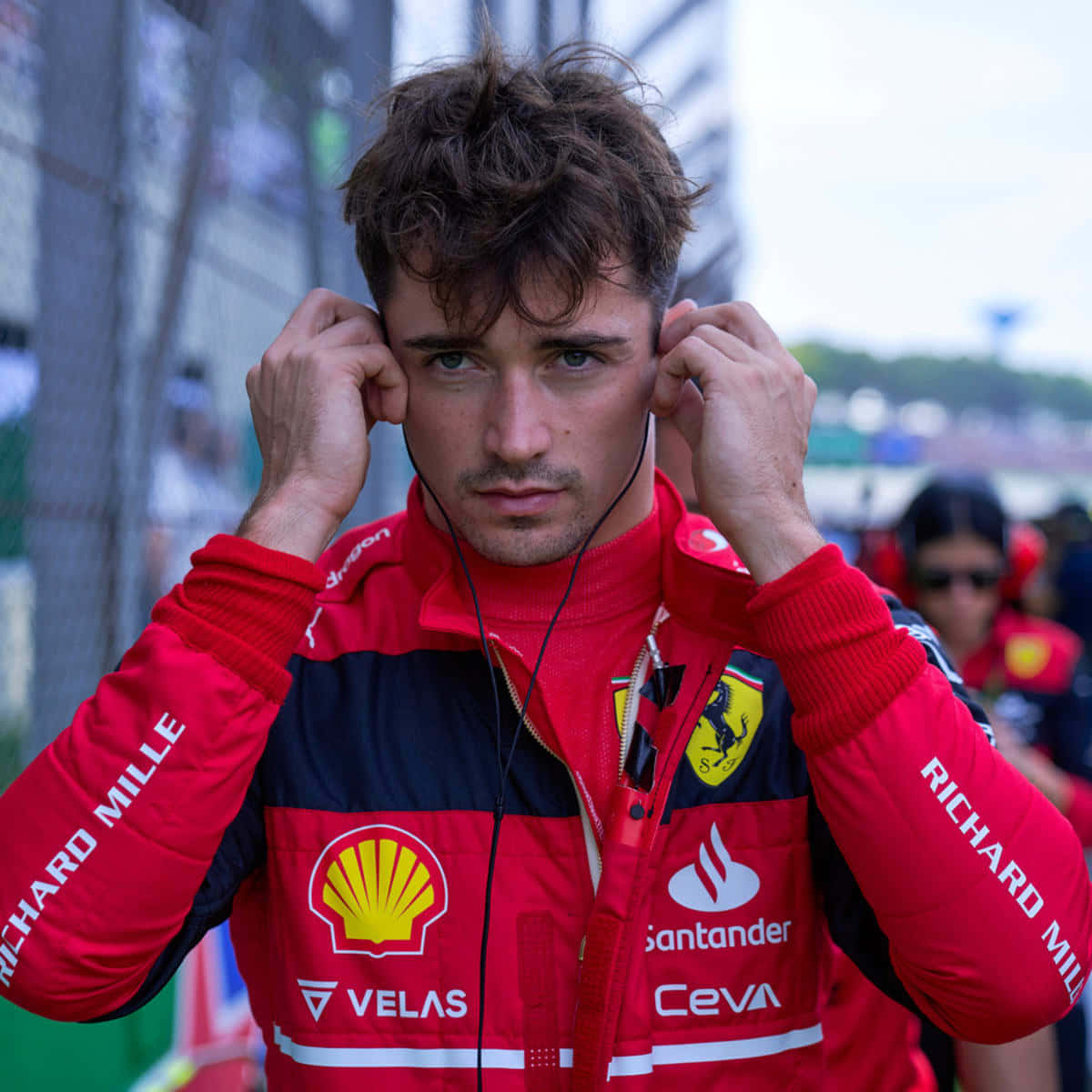 F1 Bahrain 桌布 壁紙 — 一位專注的F1車手穿著紅色法拉利車隊外套，在賽道上調整耳機。