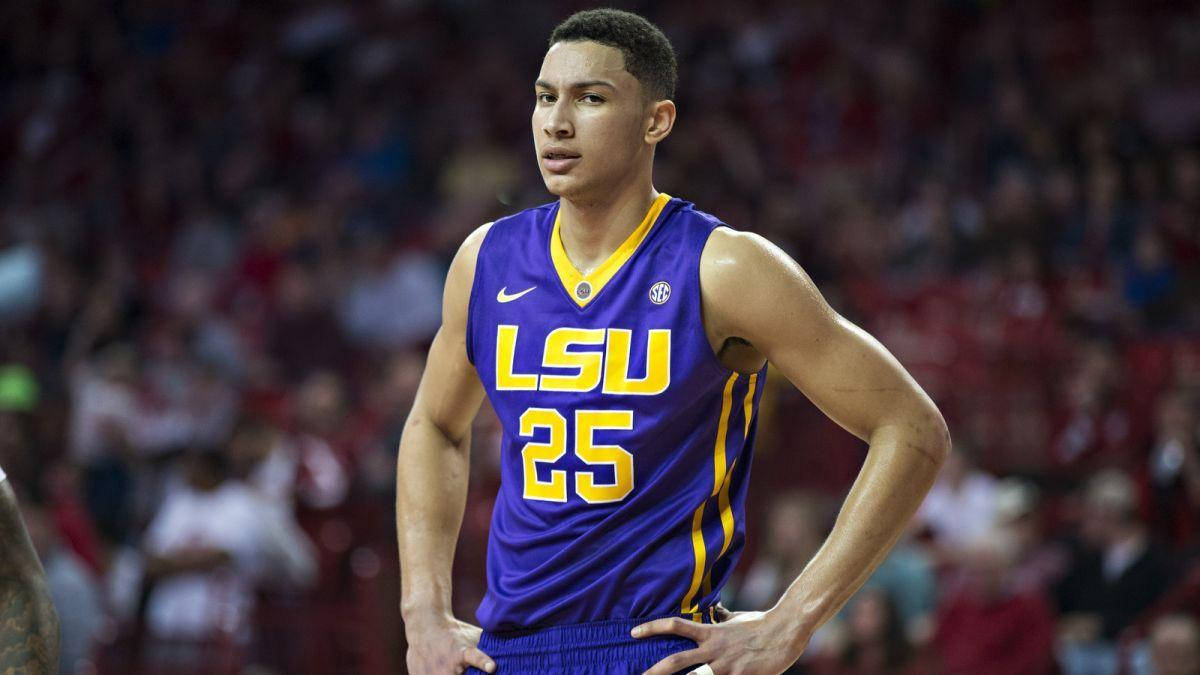 Ben Simmons 桌布 壁紙 — 一位專注的LSU籃球運動員穿著紫色和金色的球衣，在明亮的場館燈光下比賽時雙手叉腰站立。