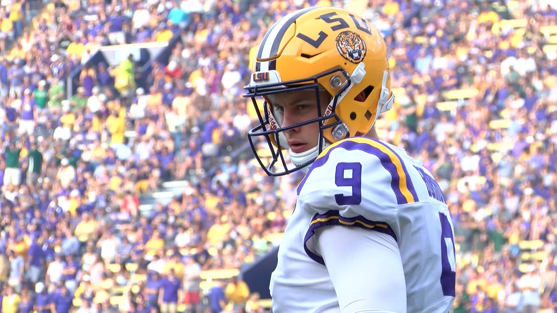 Joe Burrow 桌布 壁紙 — 一位專注的LSU美式足球員，戴著黃色頭盔、身穿白色球衣，站在球場上，背景是座無虛席的體育場人群。