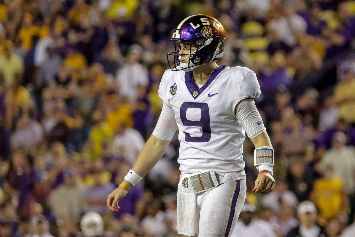 Joe Burrow 桌布 壁紙 — 一位專注的LSU美式足球四分衛，身穿白色和紫色9號球衣，站在球場上，體育場燈光下，背景是模糊的球迷。