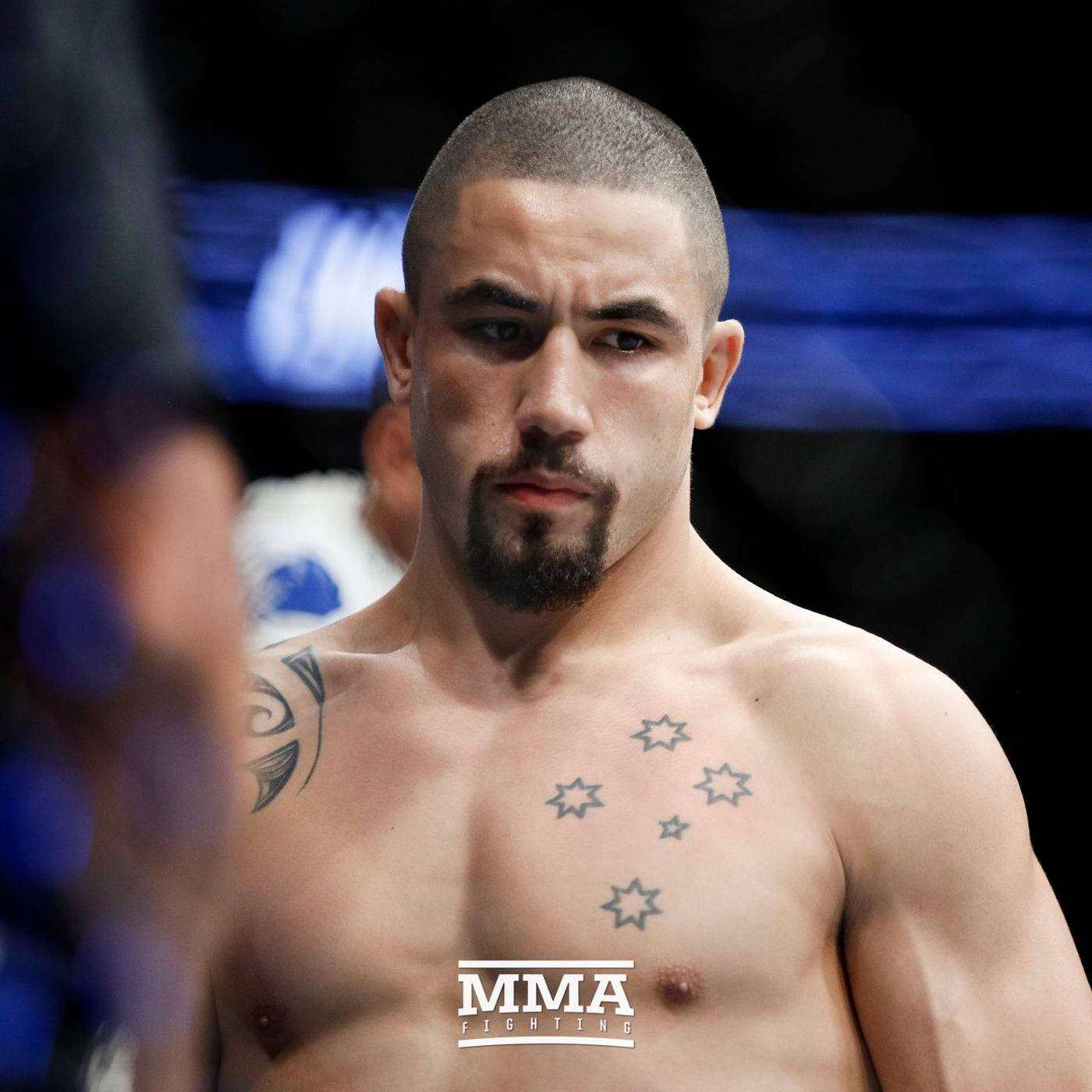 UFC 桌布 壁紙 — 一位專注的MMA拳手，身上有星星刺青，在明亮的場館燈光下於八角籠內凝視。