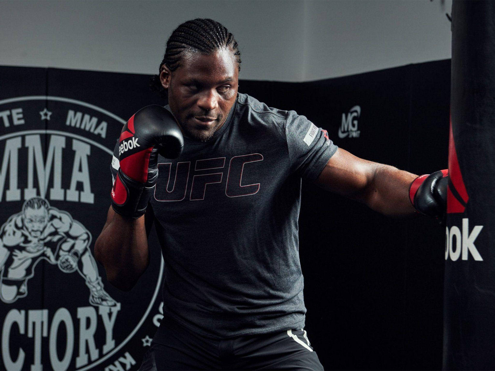 MMA 桌布 壁紙 — 一位專注的MMA拳手穿著UFC裝備，在昏暗的健身房中向沙包出拳，牆上有品牌標誌。