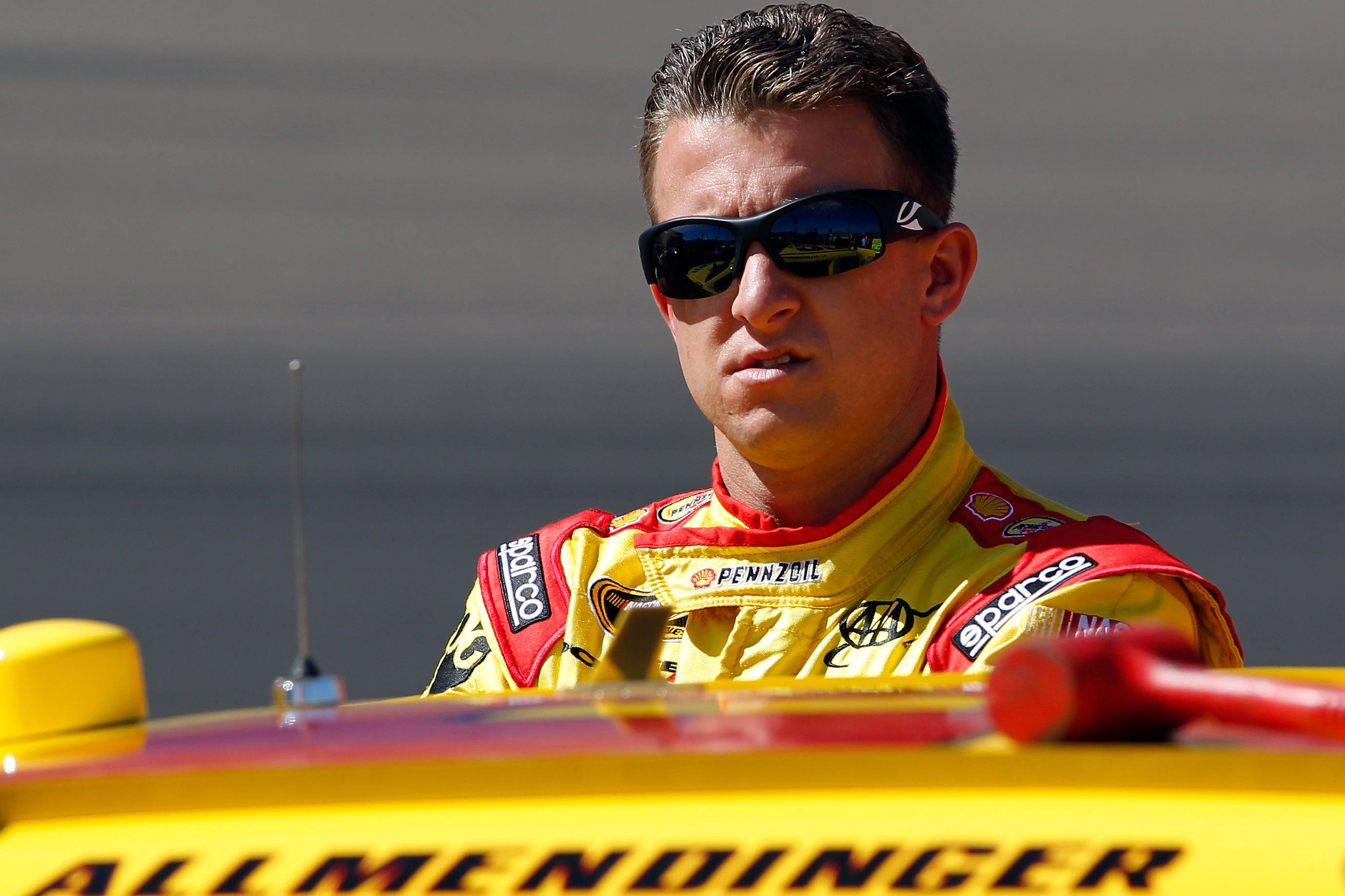 運動 桌布 壁紙 — 一位專注的NASCAR車手穿著黃紅賽車服，在晴朗的日光下從他的亮黃色賽車中探出身子。