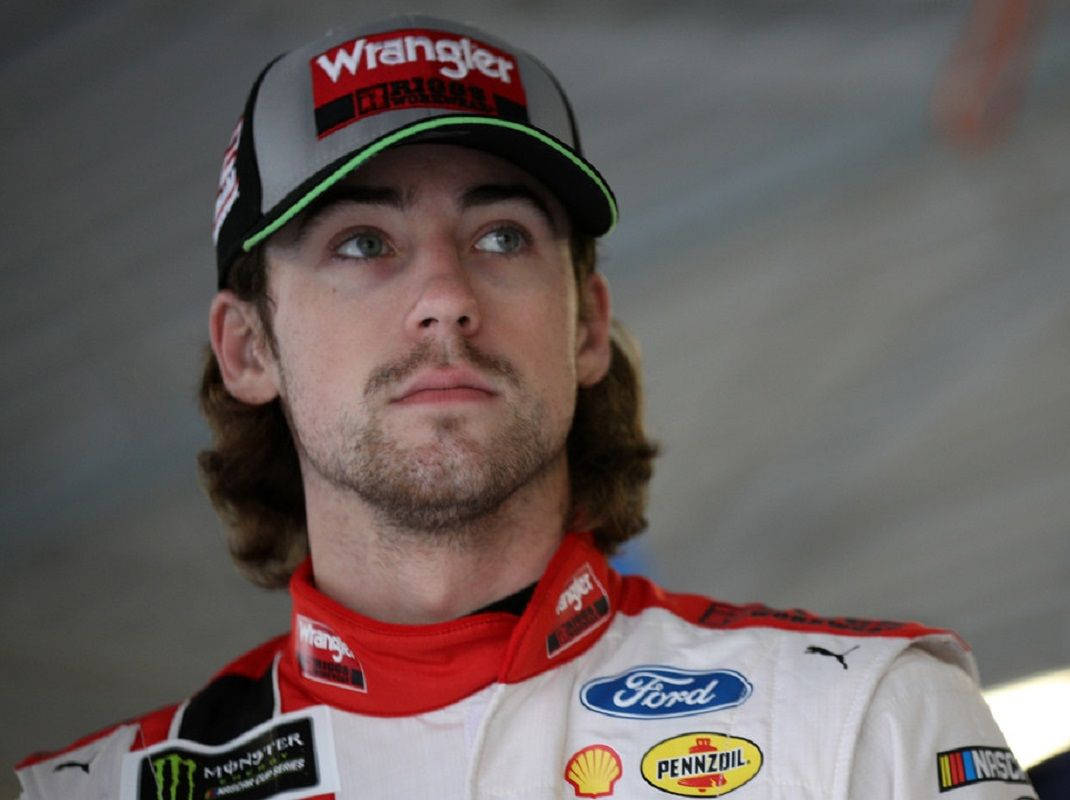 Ryan Blaney 桌布 壁紙 — 一位專注的NASCAR車手身穿Ford賽車服和Wrangler帽子，決心向上凝視。