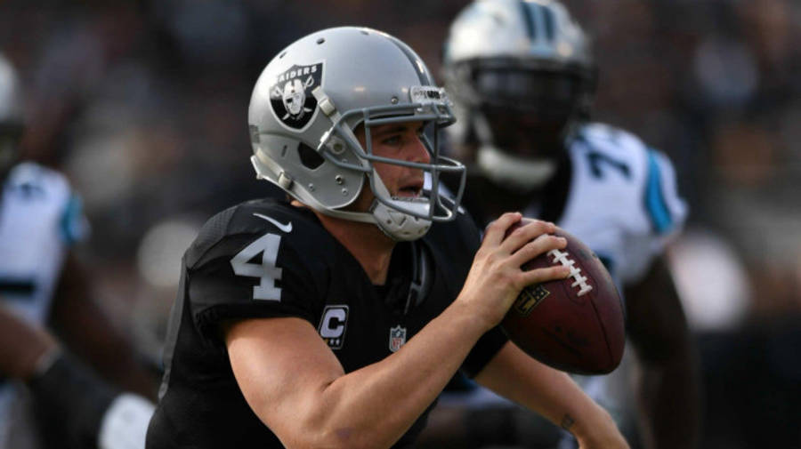 黑色 桌布 壁紙 — 一位專注的NFL四分衛，身穿黑色球衣和銀色頭盔，在日間比賽中準備投擲橄欖球。