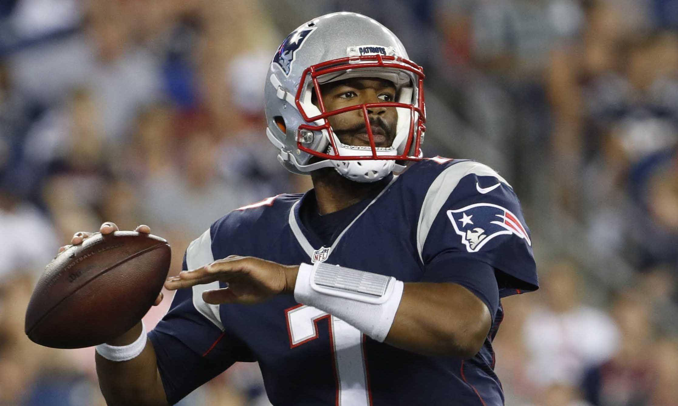 桌布 壁紙 — 一位專注的NFL四分衛穿著新英格蘭愛國者隊制服，在體育場燈光下的比賽中準備投擲橄欖球。