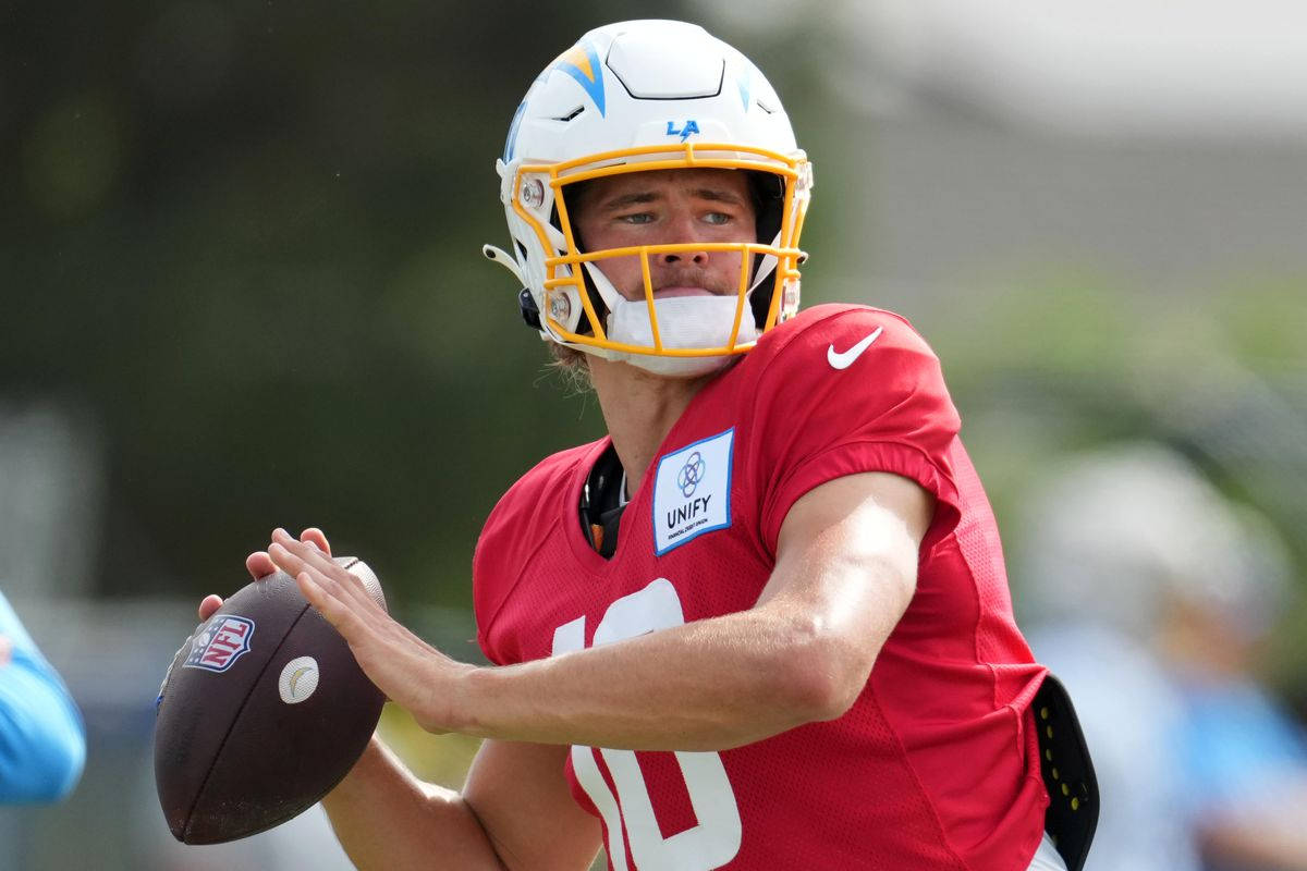 Herbert 桌布 壁紙 — 一位專注的NFL四分衛穿著紅色球衣和白色頭盔，在陽光明媚的戶外練習中準備投擲橄欖球。