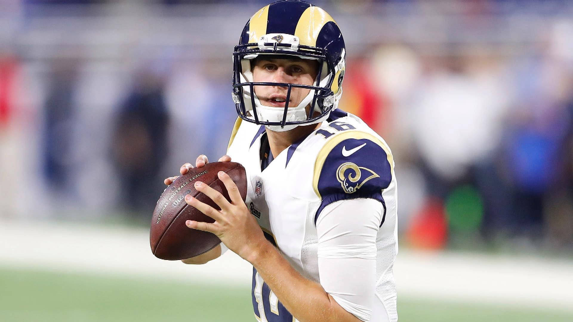 運動 桌布 壁紙 — 一位專注的NFL四分衛身穿洛杉磯公羊隊制服，在體育場燈光下準備在比賽中擲出橄欖球。