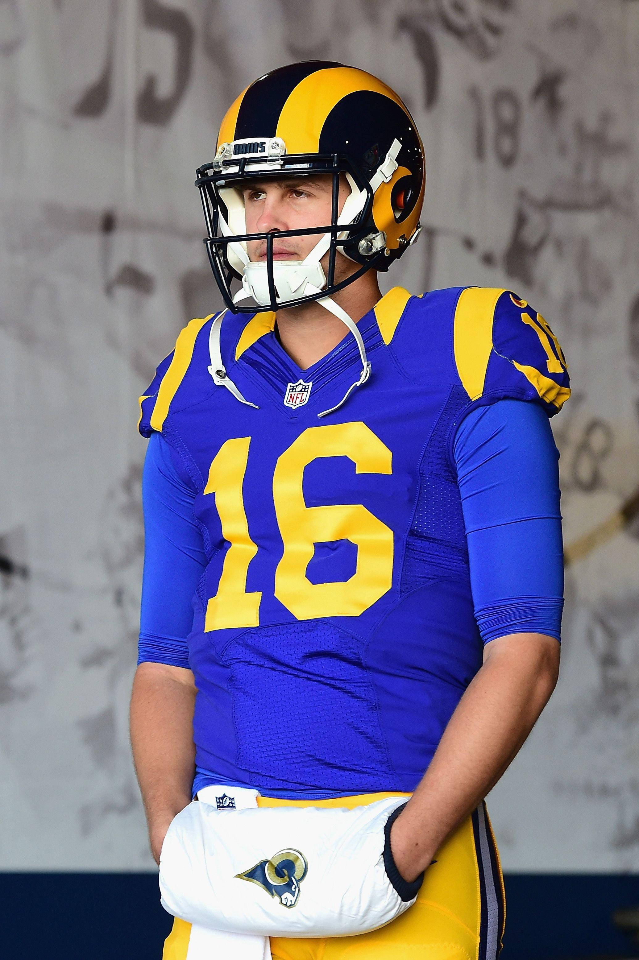 運動 桌布 壁紙 — 一位專注的NFL四分衛身穿藍金色公羊隊16號球衣，站在體育館通道中。