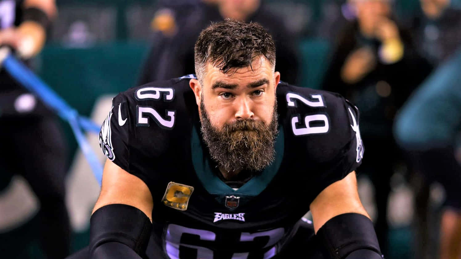 Jason Kelce 桌布 壁紙 — 一位專注的NFL球員，留著濃密鬍鬚，身穿黑色Eagles球衣，在球場上激烈地蹲伏。