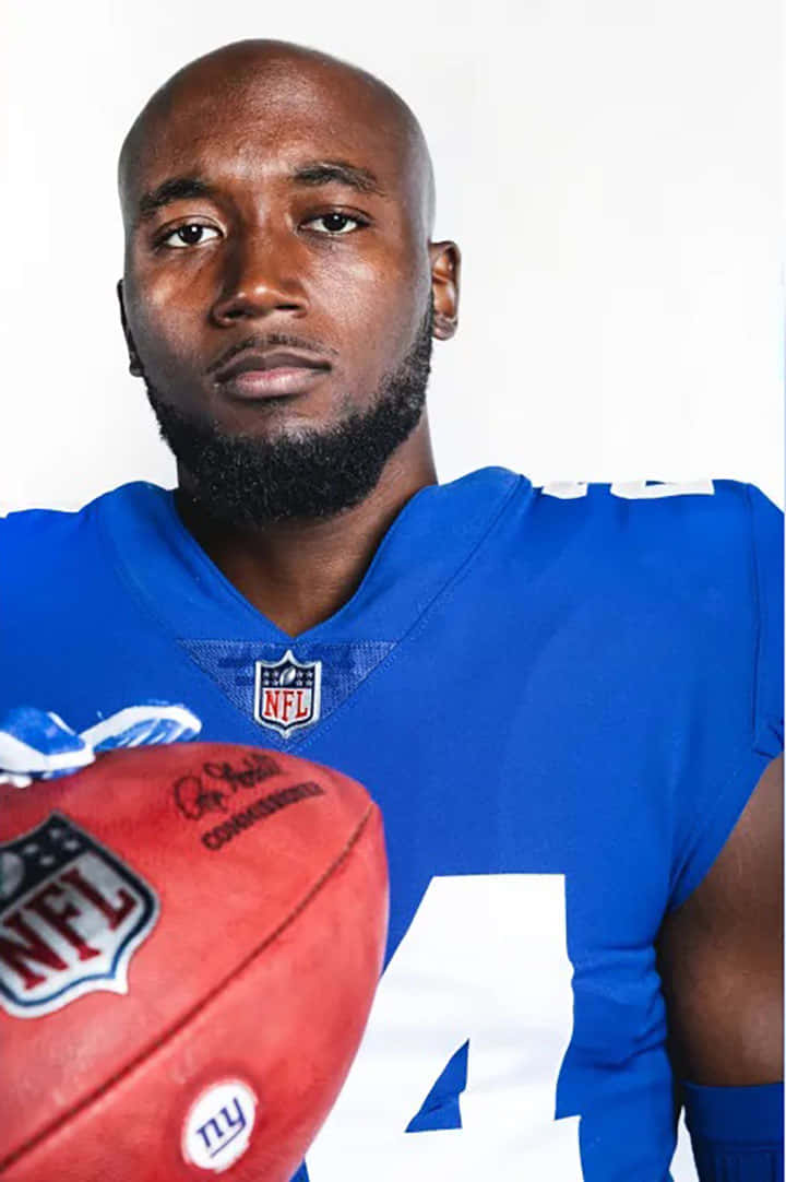 James Bradberry 桌布 壁紙 — 一位專注的NFL美式足球員身穿藍色球衣，在純白背景前手持紅色美式足球。