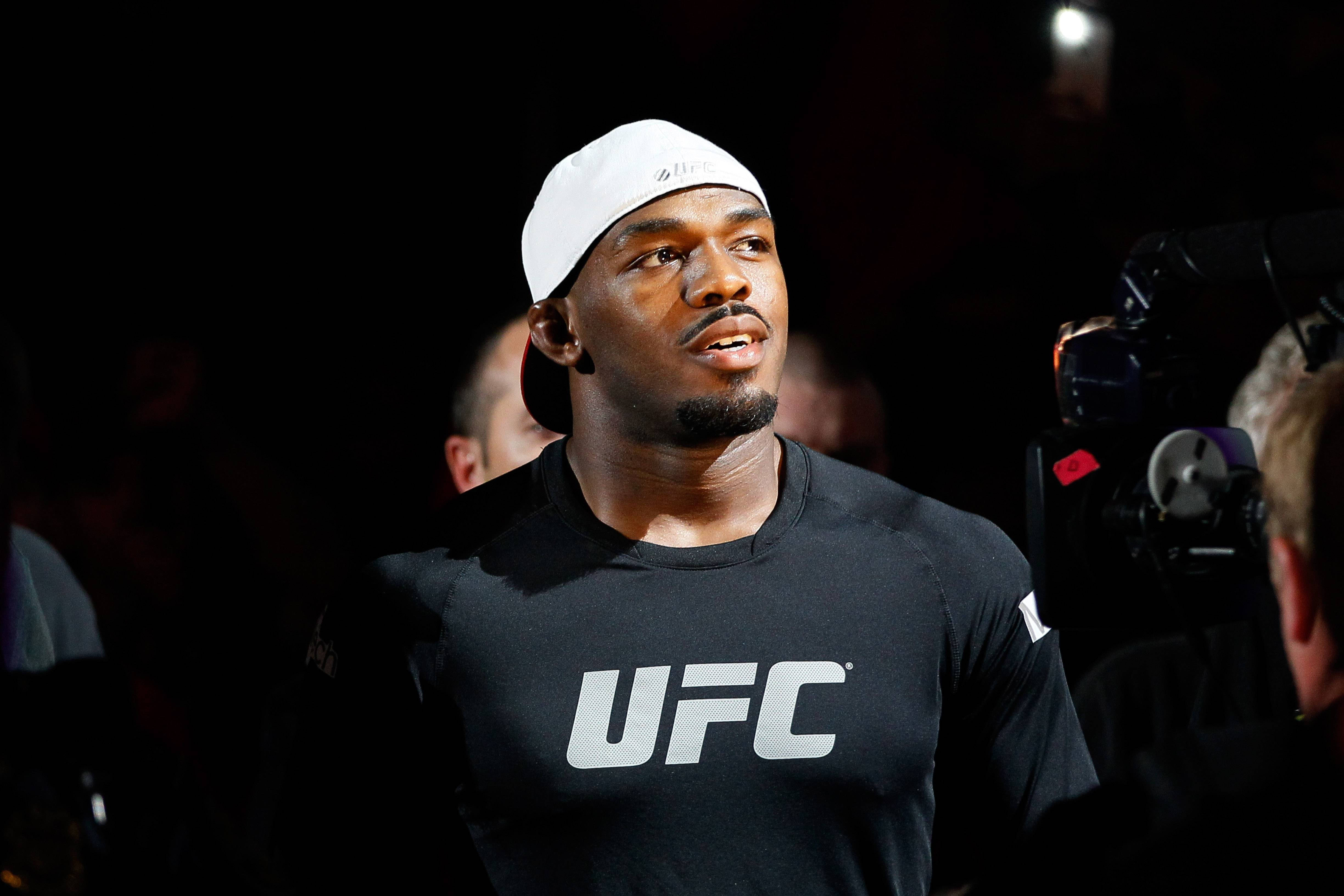 UFC 桌布 壁紙 — 一位專注的UFC拳手，身穿黑色襯衫和白色帽子，站在明亮的燈光下，周圍有攝影機。